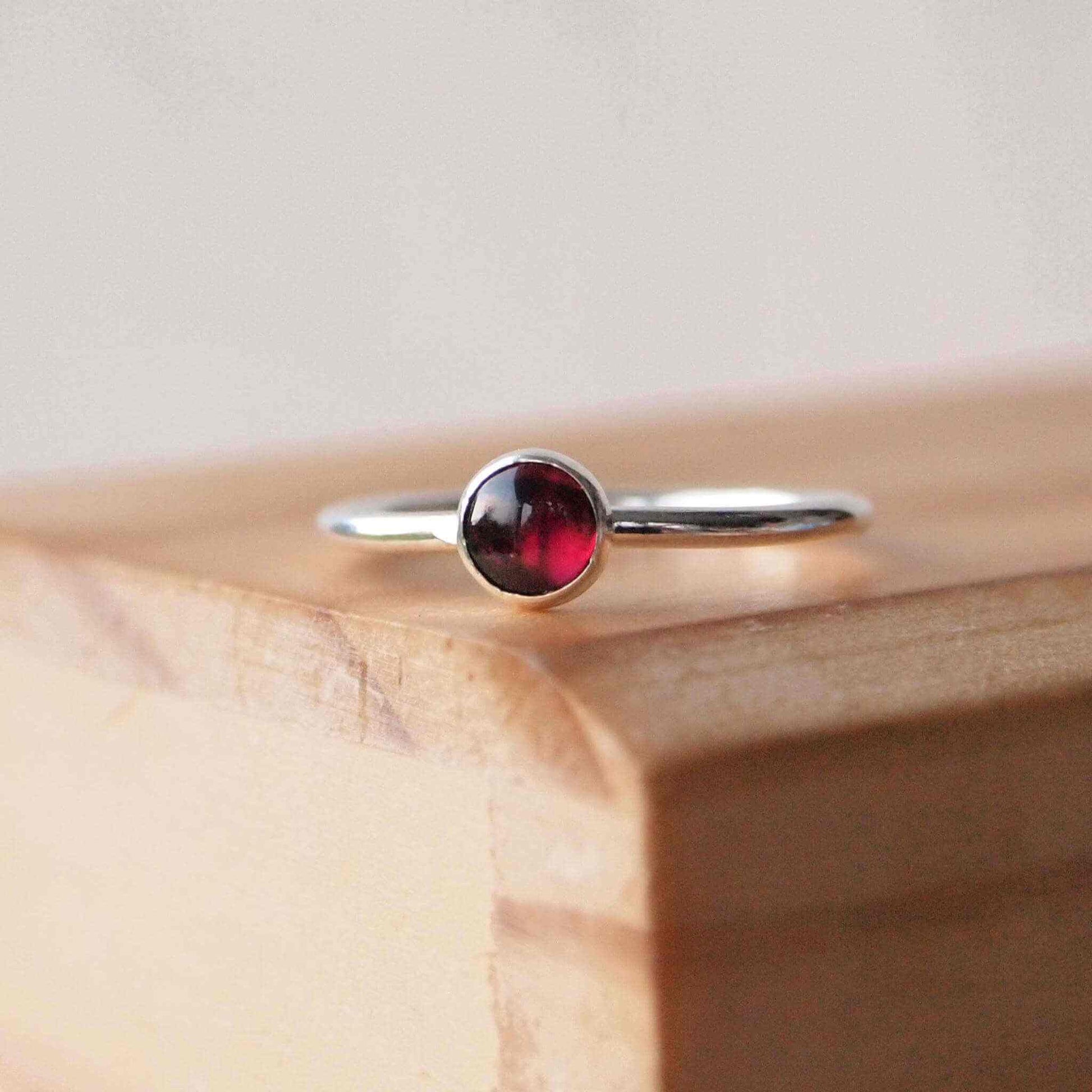 Garnet and Sterling Silver January Birthstone Ring. A 5mm round deep red garnet cabochon set very simply onto a round band of sterling silver in a minimalist style with no decoration. Handmade by maram jewellery in Scotland