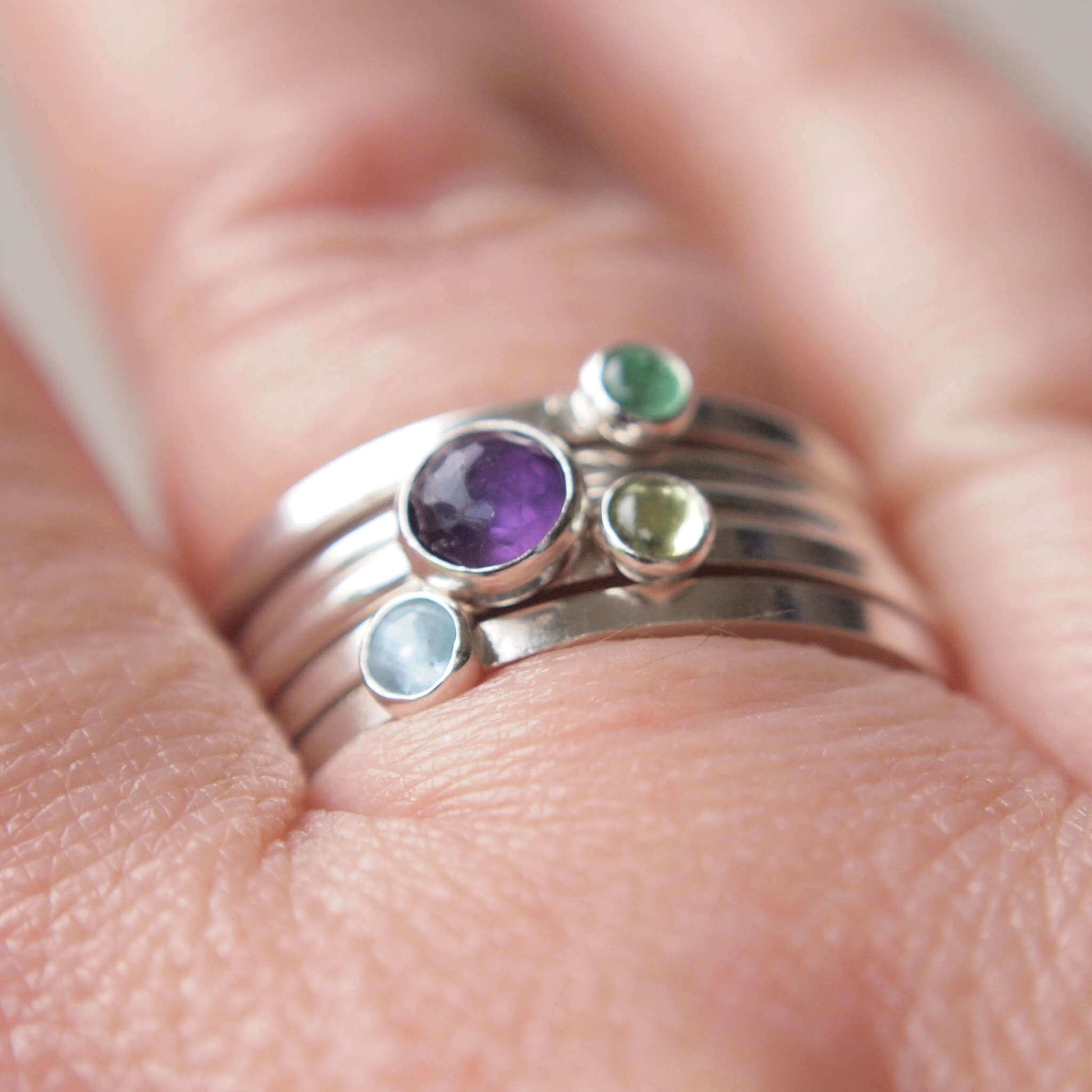 Ring set featuring four birthstones in purple, aqua, and green. The stones used are Amethyst for February, Aquamarine for March, Peridot for August and Emerald for May. The rings are made from sterling silver in a selection of band styles and different sized stones. Handmade in Scotland by maram jewellery