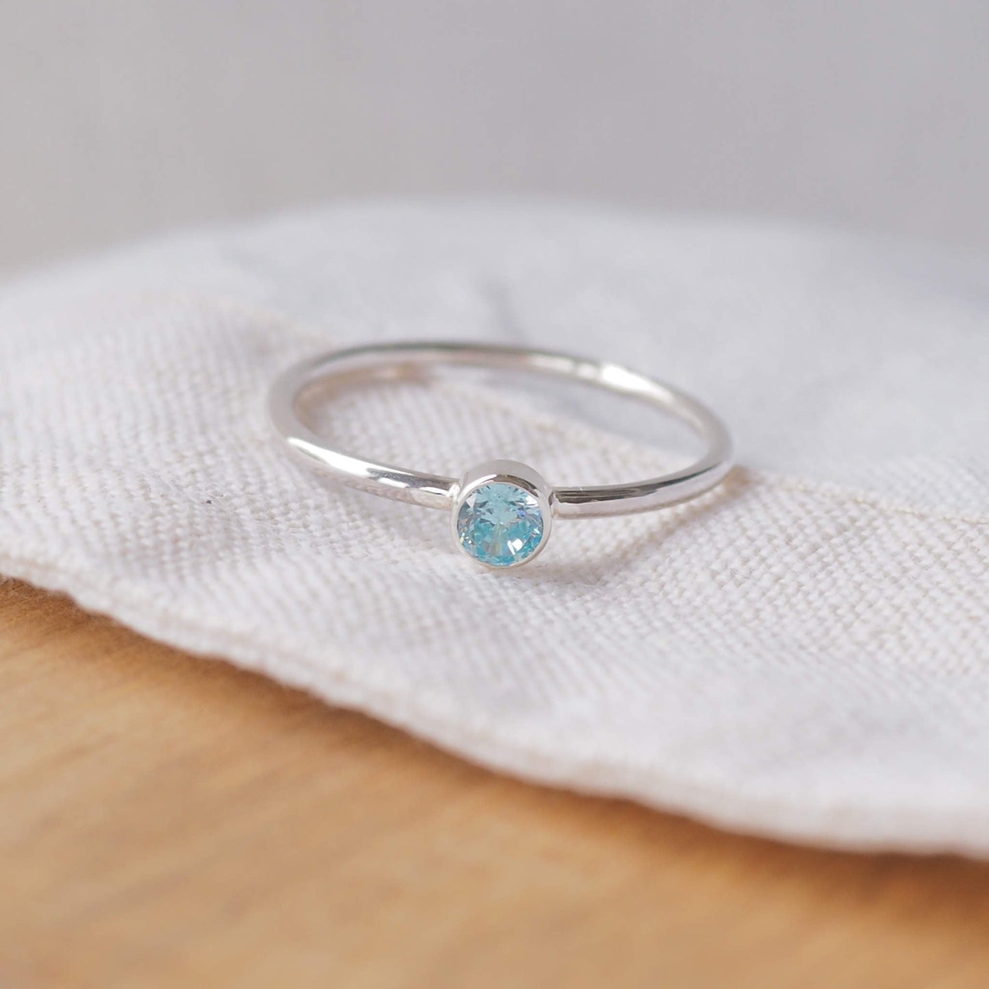 Silver ring with a light aqua gemstone. The ring is simple in style with no embellishment , with a round wire band 1.5mm thick with a simple Pale Blue Aquamarine 4mm round cubic zirconia stone set in an enclosed silver setting. Aquamarine is the birthstone for March. The ring is Sterling Silver and made to your ring size. Handmade in Scotland by Maram Jewellery