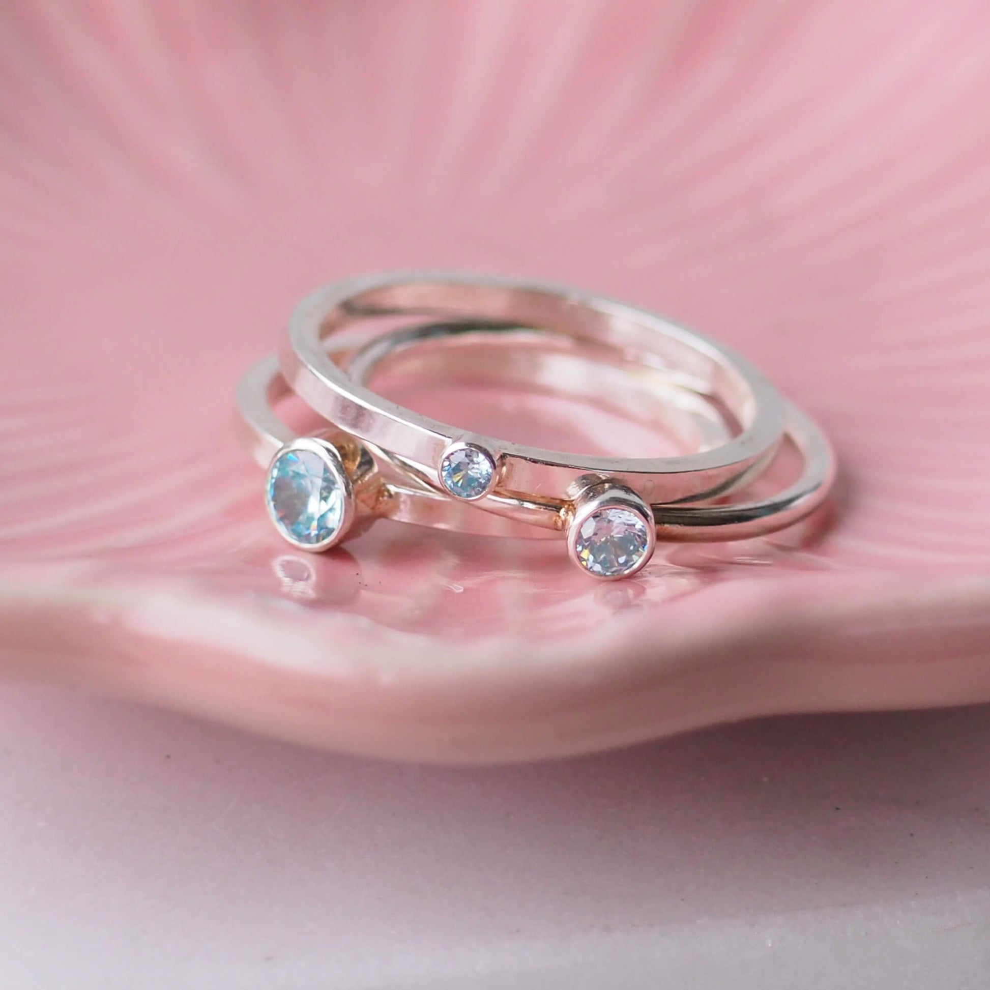 Set of three Aquamarine cubic zirconia rings loose on a delicate pink plate. Handmade by maram jewellery in Scotland UK