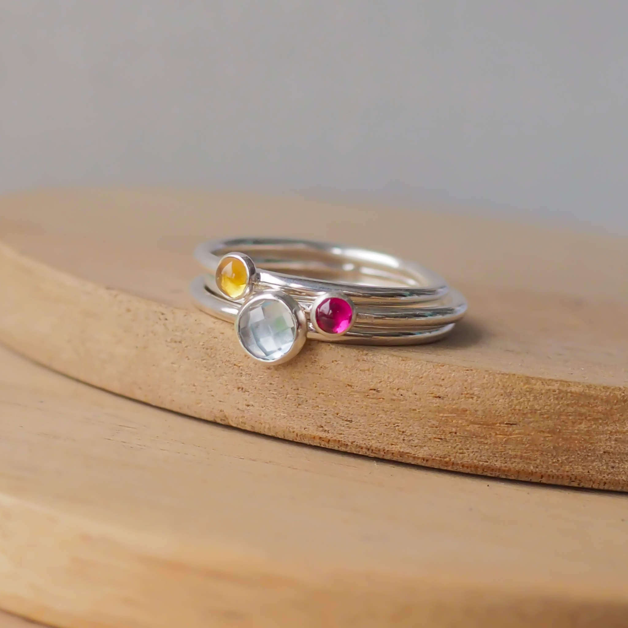 Three Birthstone RIng set with Blue Topaz, Citrine and Lab Ruby to mark March, November and July Birthdays. The three rings are made with Sterling Silver and a 5mm blue round cabochon, with two further rings with 3mm round gems in a Red Pink Lab Ruby and yellow citrine. Handmade in Scotland by maram jewellery
