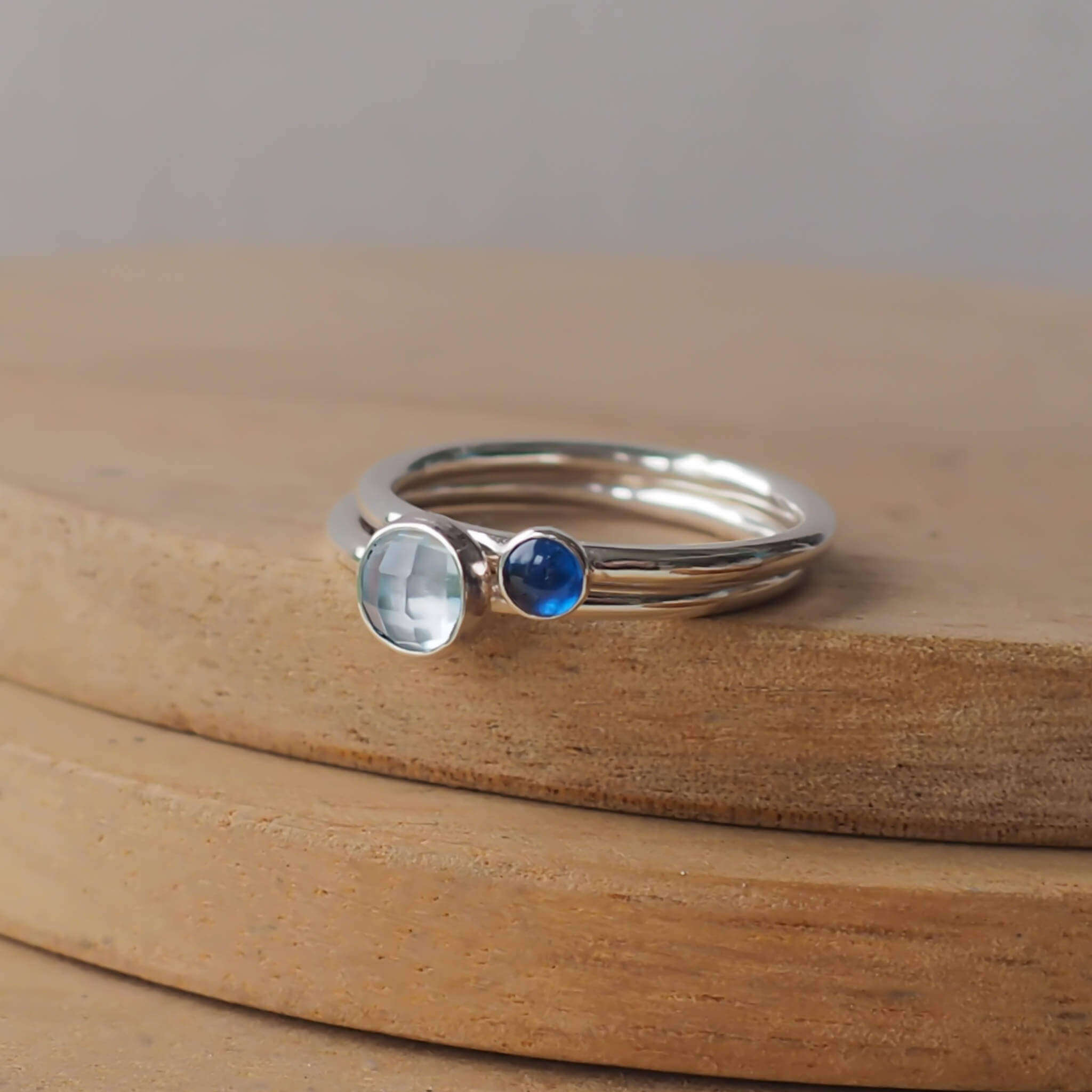 Two Birthstone Ring set with Blue Topaz and Lab Sapphire to mark March and September Birthdays. The three rings are made with Sterling Silver and a 5mm blue round cabochon, with a further rings with 3mm round gem in a blue lab sapphire . Handmade in Scotland by maram jewellery