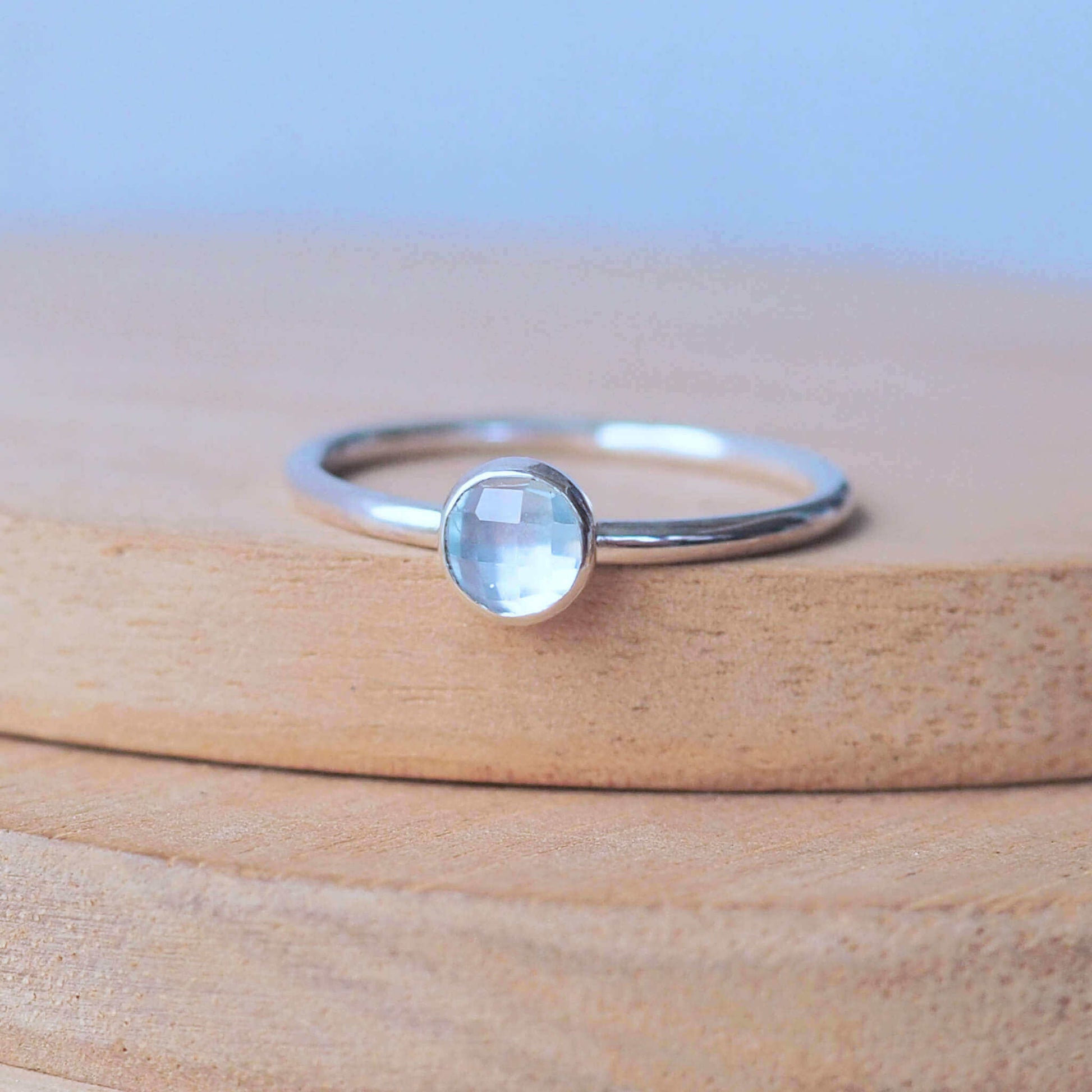 Single solitaire sterling silver ring with a round 5mm pale Blue Topaz. The ring is made in a modern simple style with a 5mm round facet cut cabochon set onto a modern halo fully round band. Made to order to your ring size, and handmade in scotland by maram jewellery