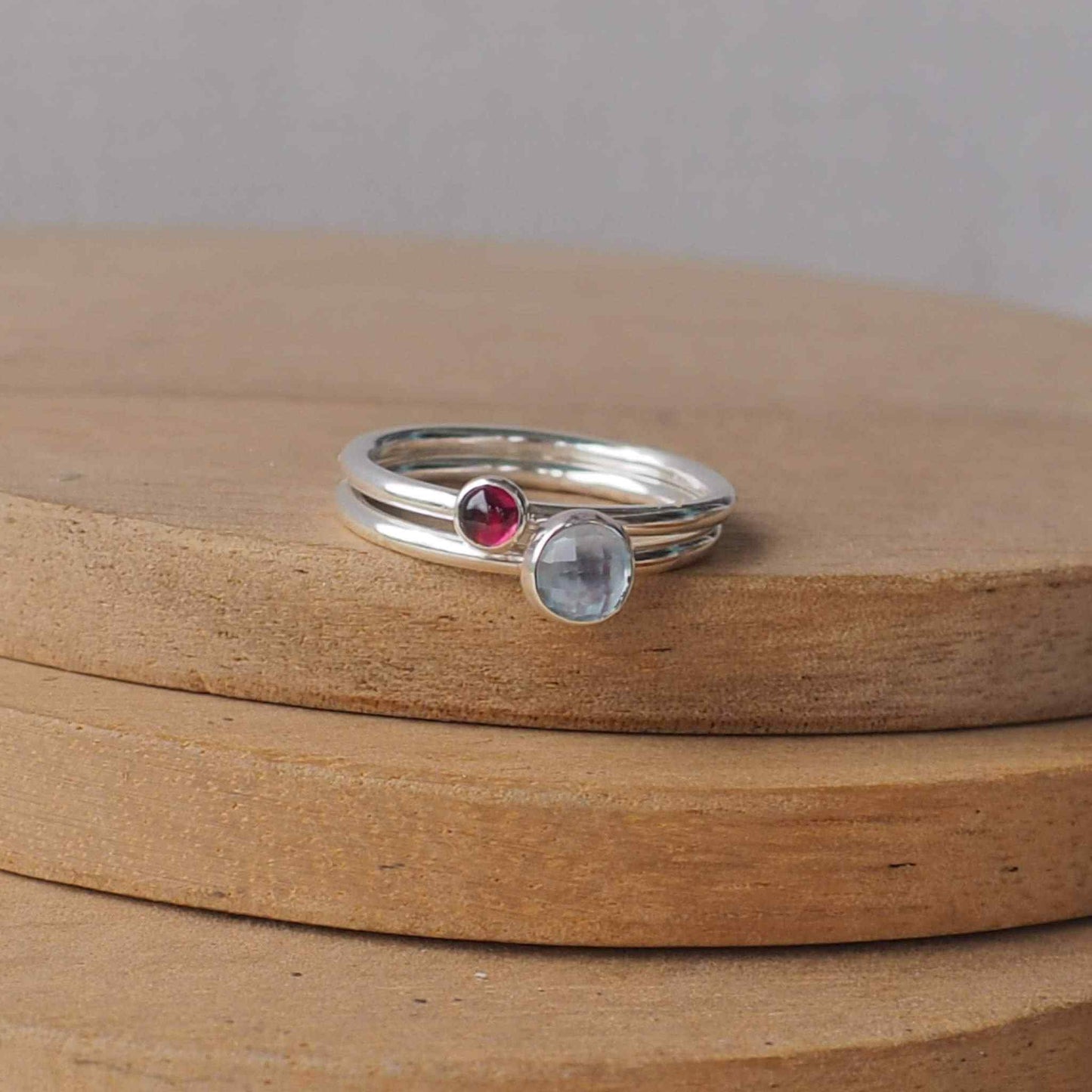 Two Birthstone Ring set with Blue Topaz and Garnet  to mark March and January Birthdays. The two rings are made with Sterling Silver and a 5mm blue round cabochon, with a further ring with 3mm round gem in a dark red garnet . Handmade in Scotland by maram jewellery