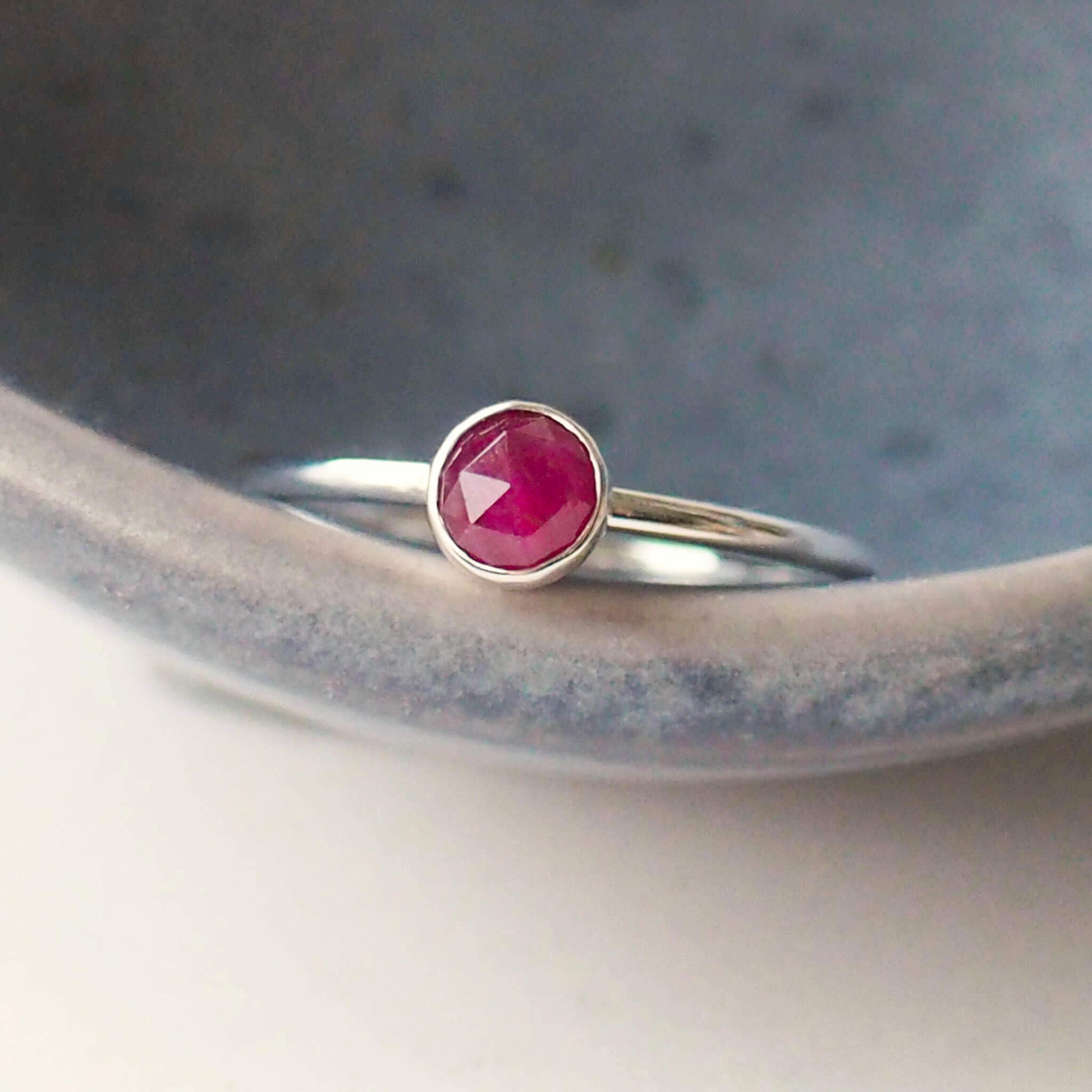 Red Ruby round gemstone ring in Sterling SIlver pictured against a grey background. The ring in minimalist in style with a round facet cut ruby in a 5mm size. Handmade by maram jewellery in Edinburgh UK