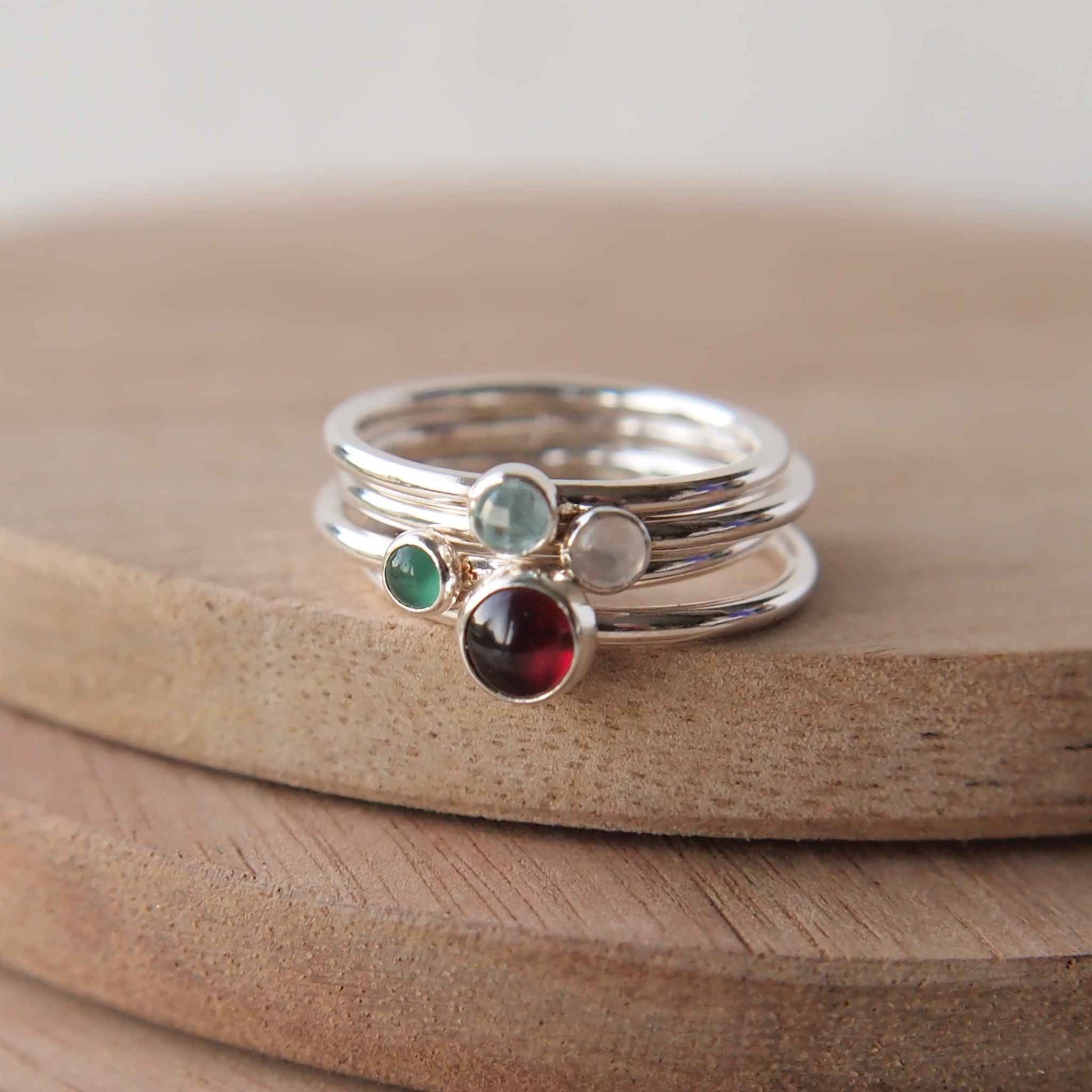 Birthstone ring set with four stones to mark family birthstones. image contains rings in sterling silver with a red garnet, green agate, white moonstone and blue topaz. Handmade by maram jewellery in Scotland UK