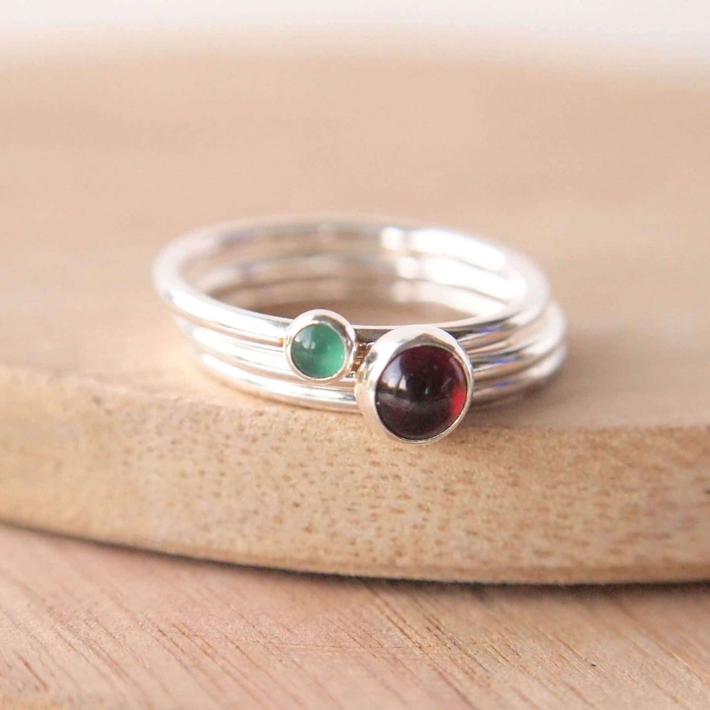 Double ring set with January and May Birthstones. January birthstone ring has a 5mm round dark red cabochon smooth cut stone, and the May birthstone is a green agate is a 3mm emerald green smooth round cabochon measuring 3mm, both are set onto individual bands of sterling silver. Handmade in Edinburgh by Maram Jewellery