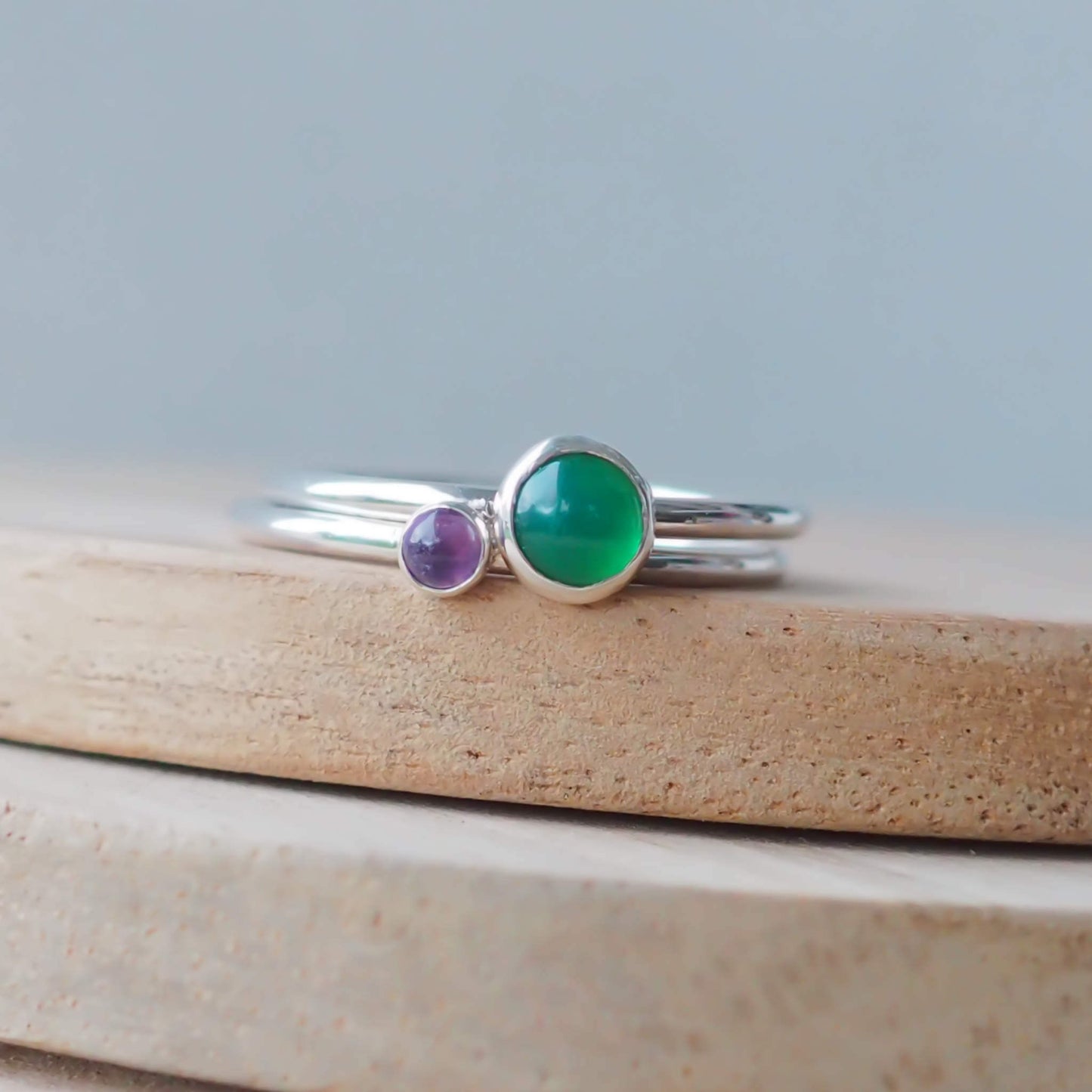 Two silver ring set with round stones. Simple round bands with a 5mm Green Agate and a 3mm Amethyst. Rings are pictured on wood background. Handmade in Scotland by Maram Jewellery