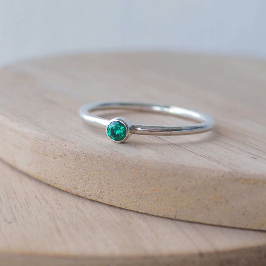 Silver ring with a bright green gemstone. The ring is simple in style with no embellishment , with a round wire band 1.5mm thick with a simple emerald green 3mm round cubic zirconia stone set in an enclosed silver setting. Emerald is birthstone for May. The ring is Sterling Silver and made to your ring size. Handmade in Scotland by Maram Jewellery