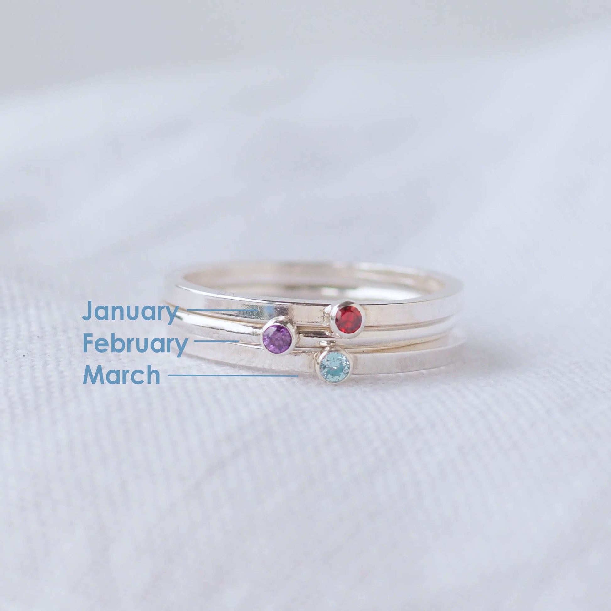 Three silver rings showing January, February and March Birthstones. The rings are simple silver bands with a miniature birthstone on the band in red, purple and aqua cubic zirconia. Handmade in Edinburgh by maram jewellery