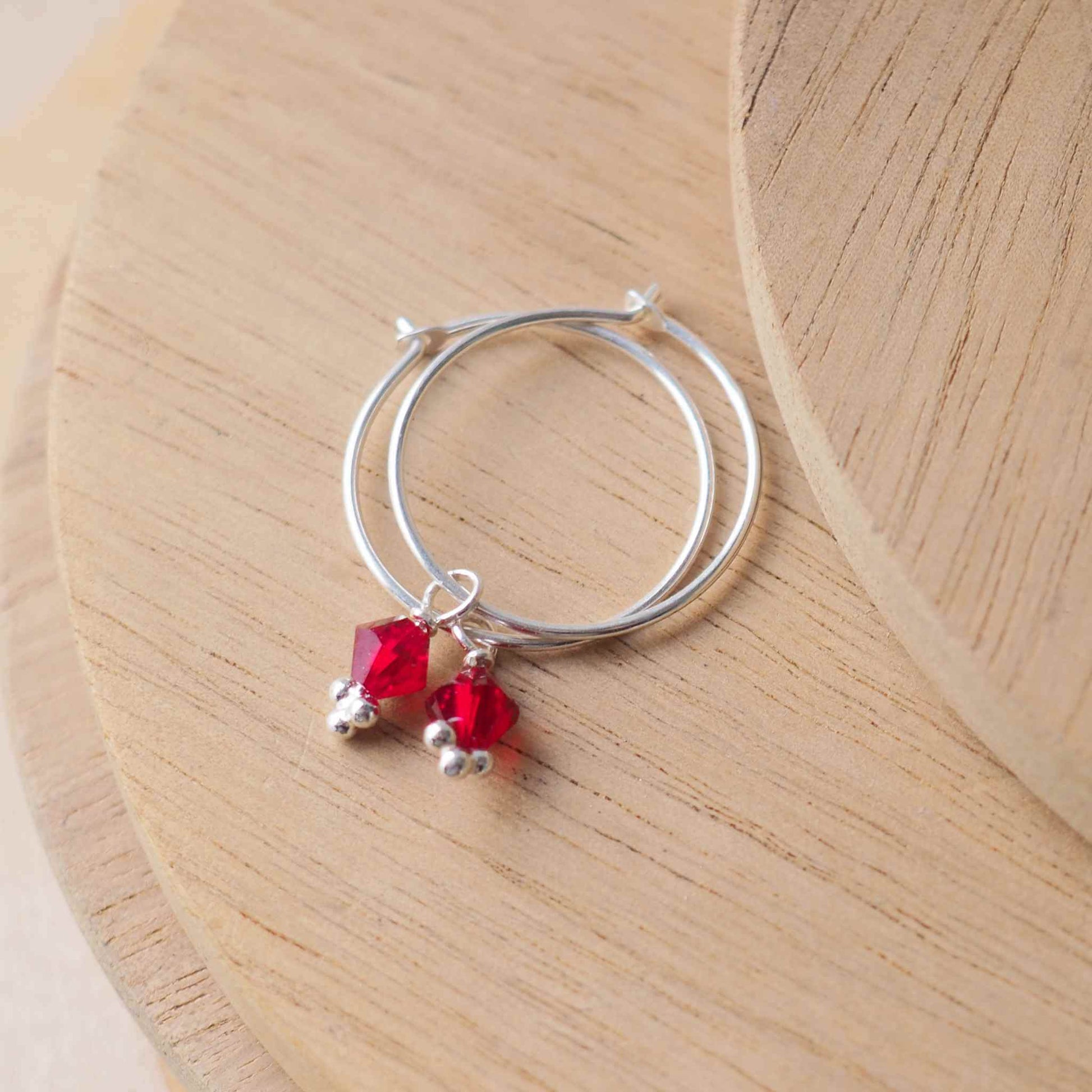 Red Garnet simple birthstone hoop earrings with a thin sterling silver wire hoop with a single small red crystal. Handmade in a small studio in Scotland UK