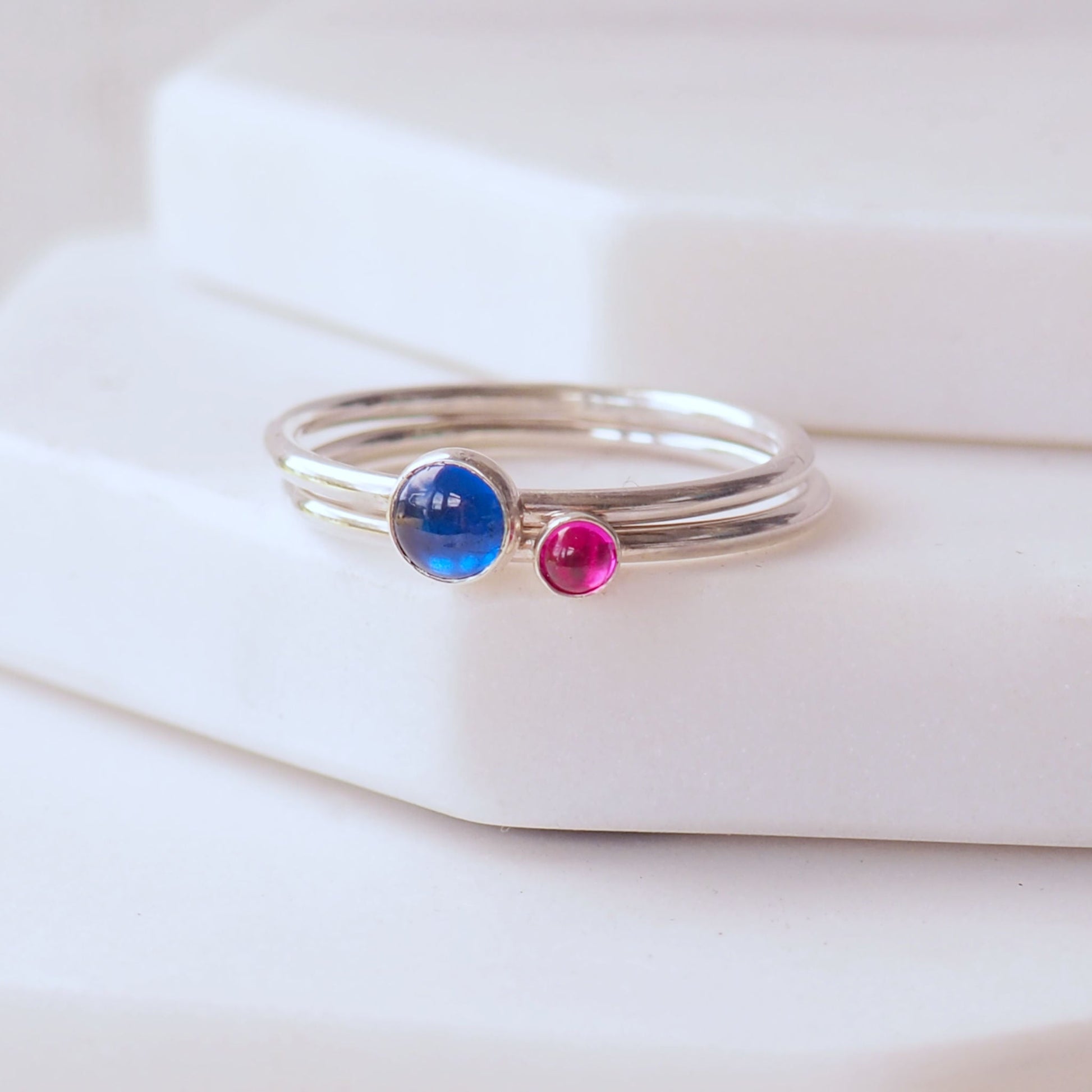 Two ring set with A september and July birthstone - a bright blue lab sapphire and a bright pink Lab Ruby. Handmade in Scotland by maram jewellery