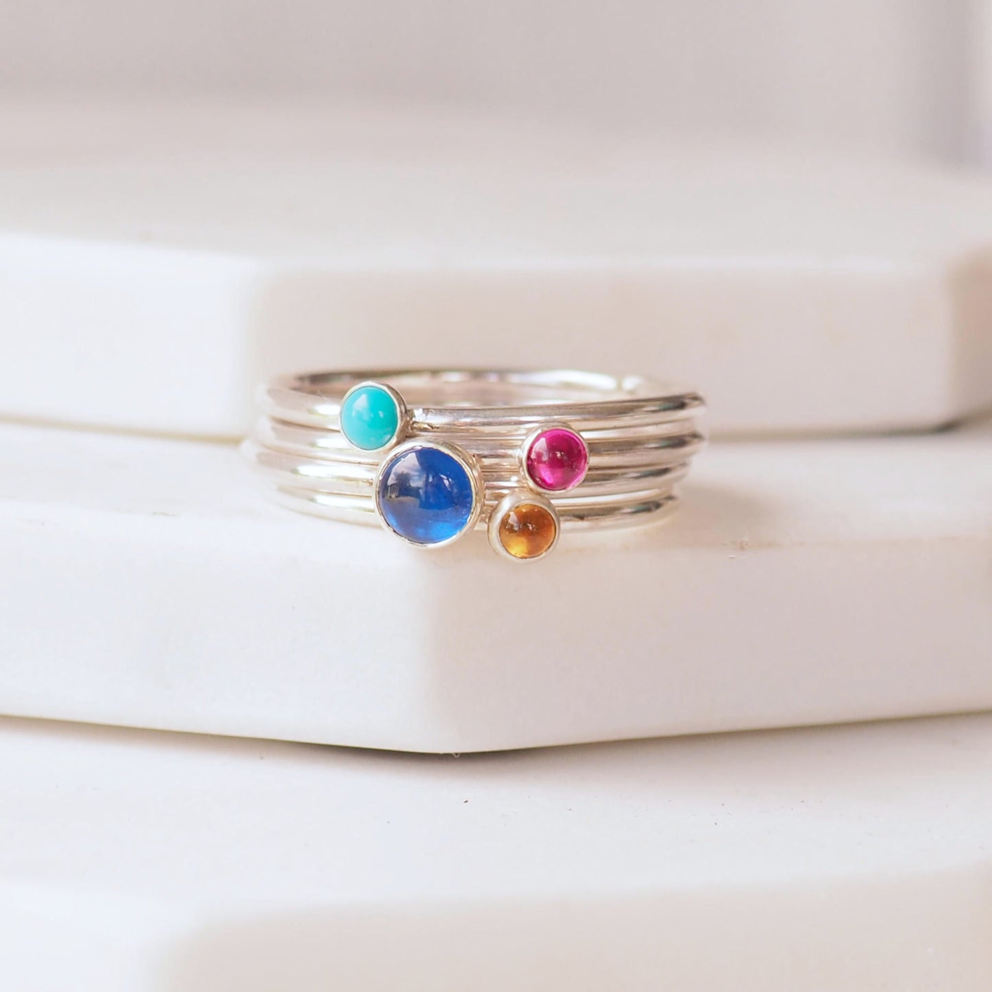 Four ring set with Lab Sapphire, Turquoise, Lab Ruby and Citrine. A colourful birthstone ring set with blue pink and yellow round gemstones. Handmade by maram jewellery in her small studio in Edinburgh UK