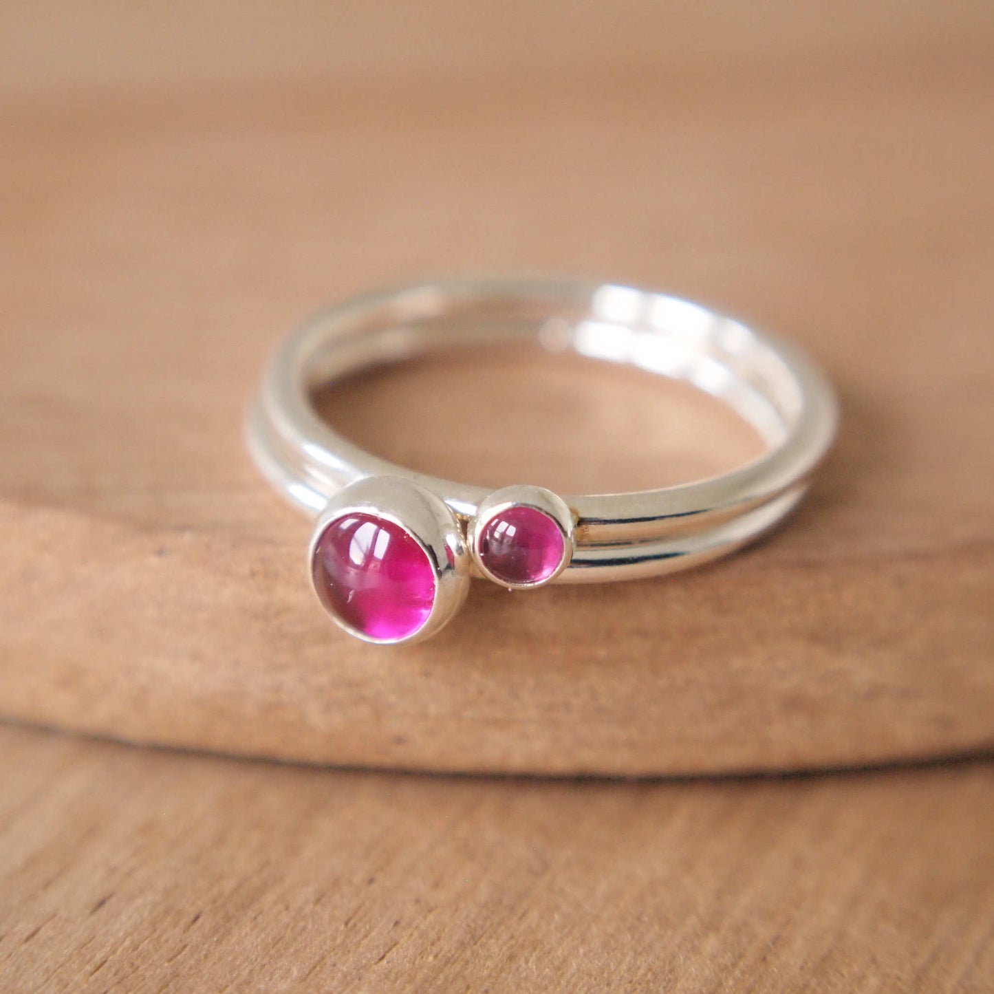 Double Ring set in Sterling Silver and hot pink Lab Ruby gemstones, The rings have two round gemstones of 5mm and 3mm size and are set simply onto round bands of sterling silver. These are July's birthstone and are handmade to your ring size by maram jewellery in Scotland
