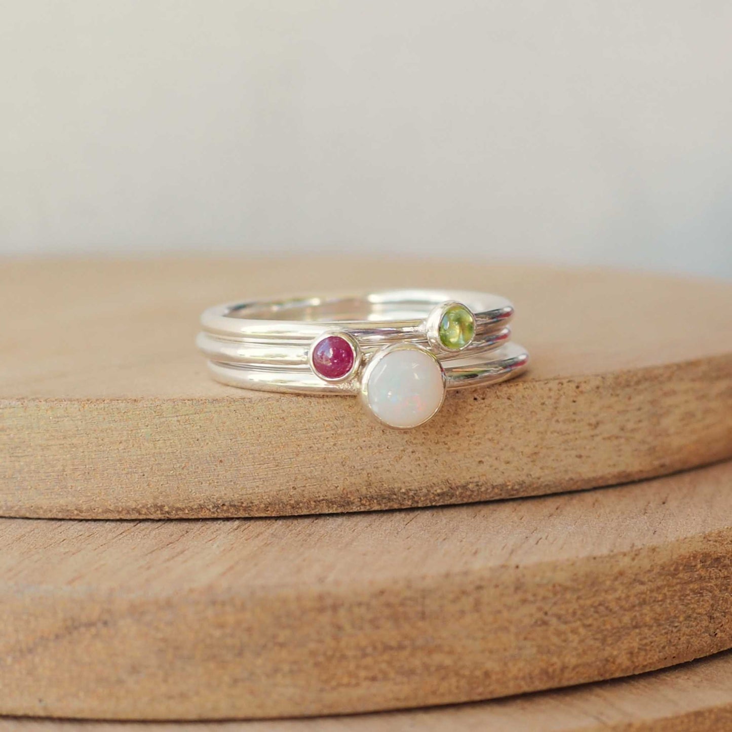 Three silver solitaire ring set with round Opal, Ruby and Peridot gemstones set onto simple round bands in a minimalist style. Handmade jewellery made in the UK