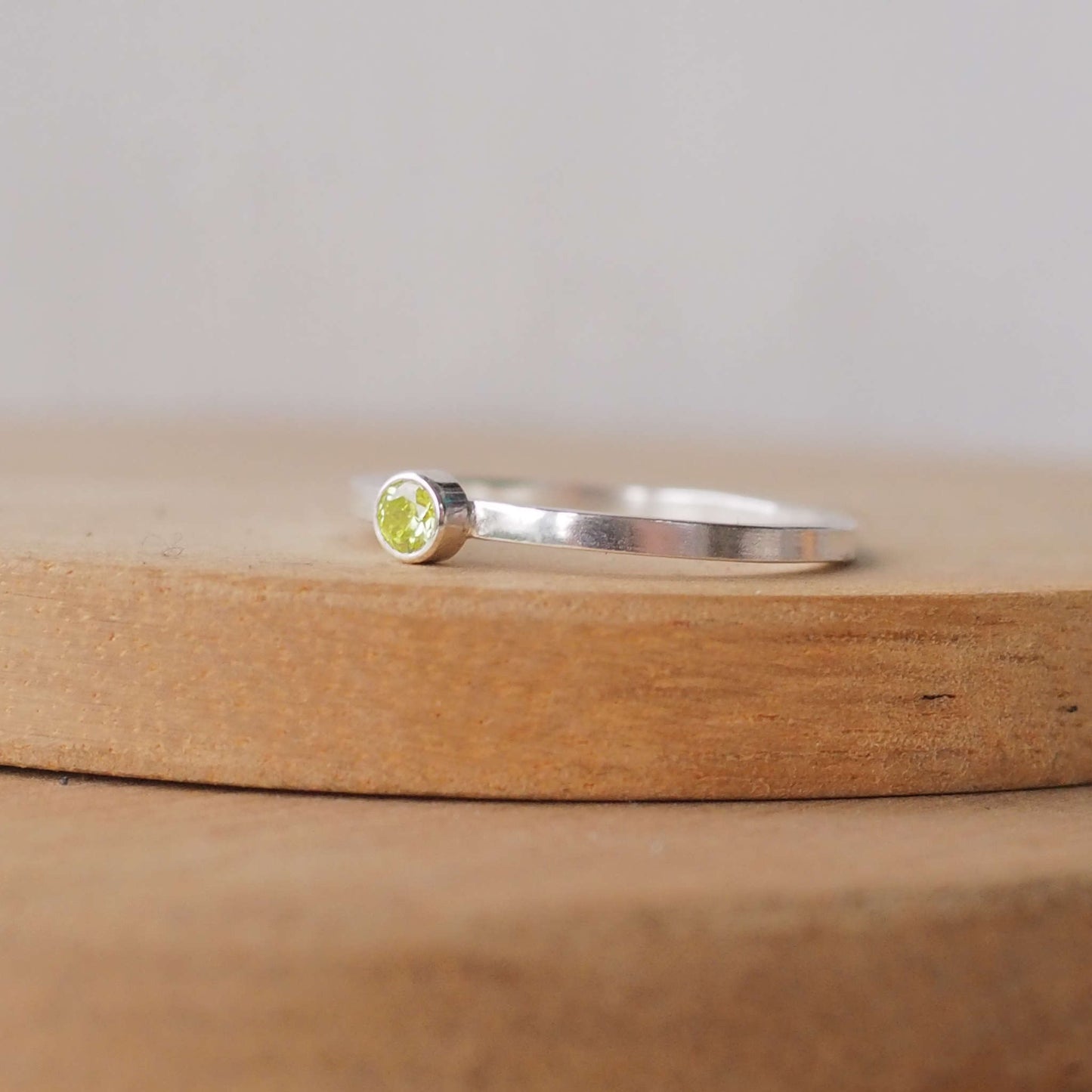 Peridot solitaire ring in a modern style with a simple square band, The ring is made from Sterling Silver and mossy green Cubic zirconia with a 4mm round gemstone fully enclosed in a silver setting. Handmade by maram jewellery in Edinburgh