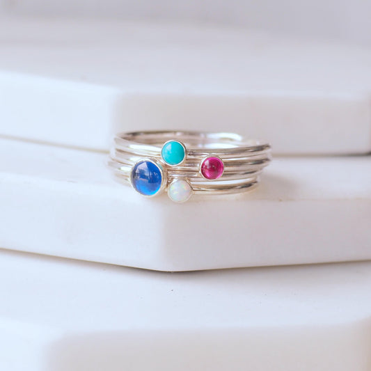 Four ring set with Lab Sapphire, Turquoise, Lab Ruby and Lab Opal. A colourful birthstone ring set with blue pink and white round gemstones. Handmade by maram jewellery in her small studio in Edinburgh UK