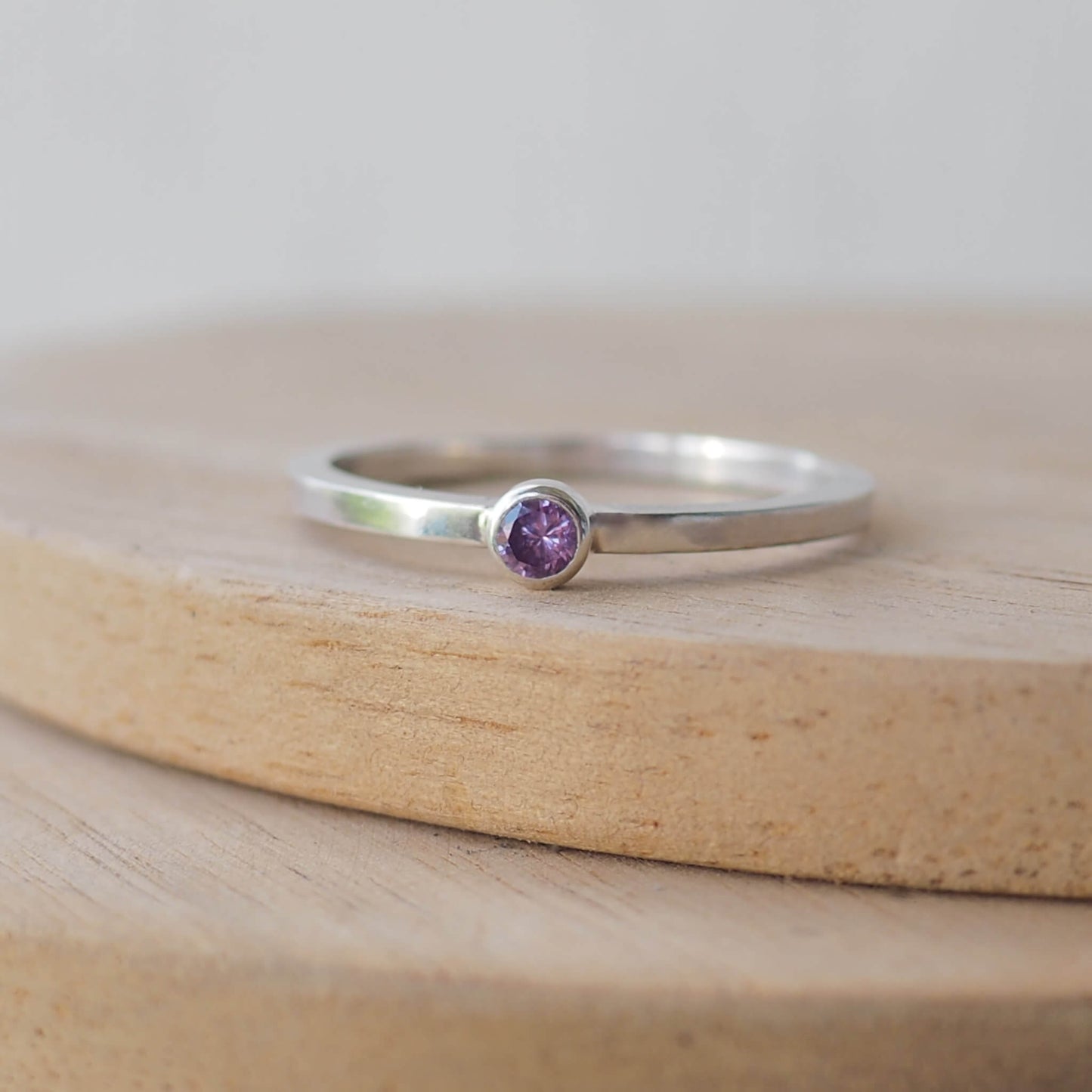 Silver ring with a purple gemstone. The ring is simple in style with no embellishment , with a square wire band 1.5mm thick with a simple purple 3mm round cubic zirconia stone set in an enclosed silver setting. Amethyst is birthstone for February. The ring is Sterling Silver and made to your ring size. Handmade in Scotland by Maram Jewellery
