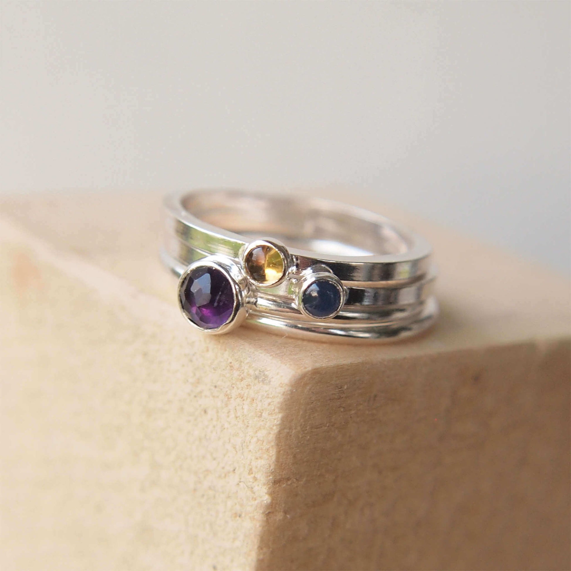 Ring set featuring three birthstones in purple, yellow and Blue. The stones used are Amethyst for February, Citrine for November, September for Sapphire. The rings are made from sterling silver in a selection of band styles and different sized stones. Handmade in Scotland by maram jewellery