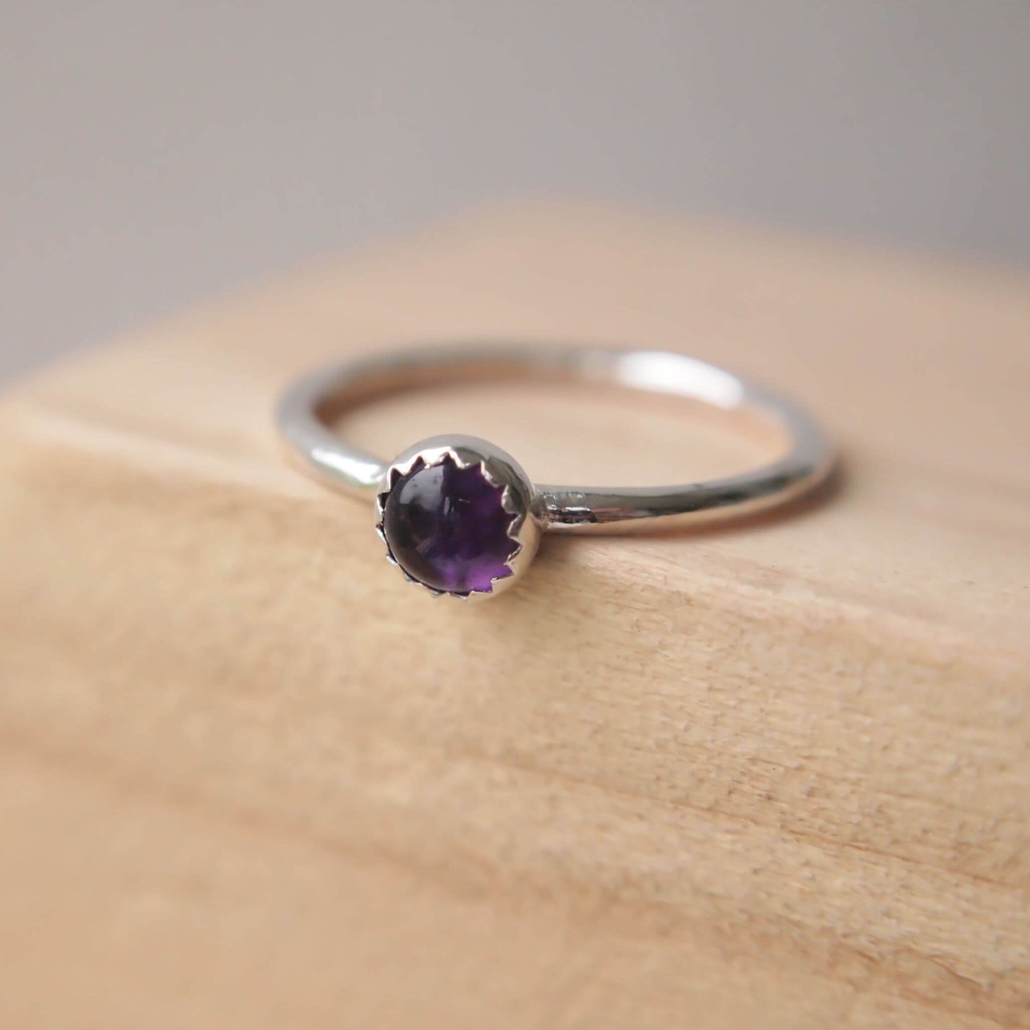 Single solitaire sterling silver ring with a round 5mm purple Amethyst. The ring is made in a modern simple style with a 5mm round cabochon set onto a modern halo fully round band. Made to order to your ring size, and handmade in scotland by maram jewellery