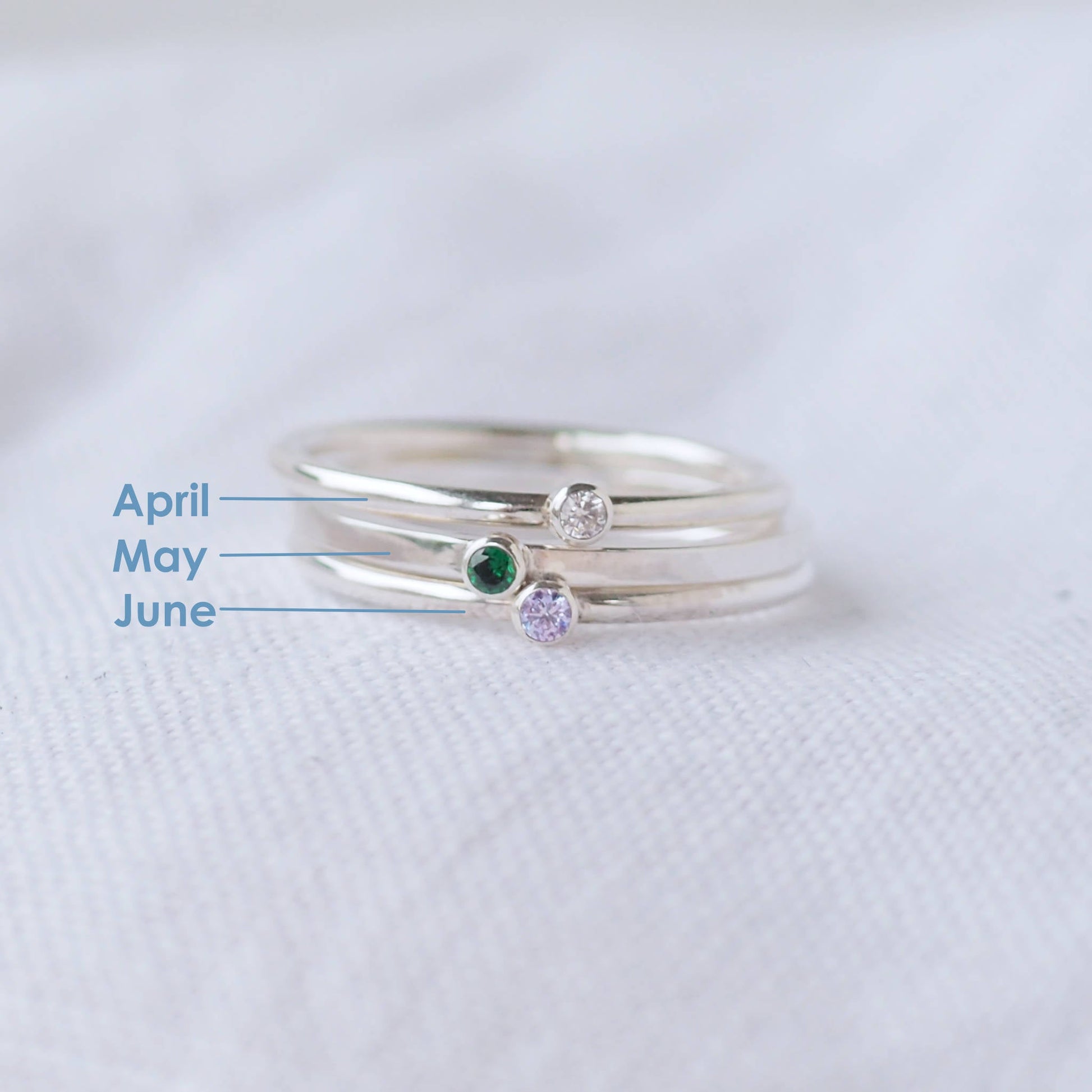 Three silver rings showing April, May and June Birthstones. The rings are simple silver bands with a miniature birthstone on the band in clear, green and pink cubic zirconia. Handmade in Edinburgh by maram jewellery