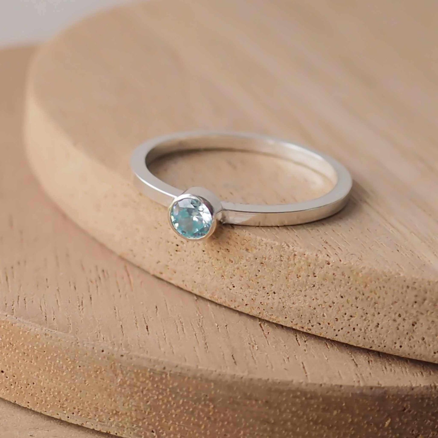Silver ring with a light aqua gemstone. The ring is simple in style with no embellishment , with a square wire band 1.5mm thick with a simple Pale Blue Aquamarine 4mm round cubic zirconia stone set in an enclosed silver setting. Aquamarine is the birthstone for March. The ring is Sterling Silver and made to your ring size. Handmade in Scotland by Maram Jewellery