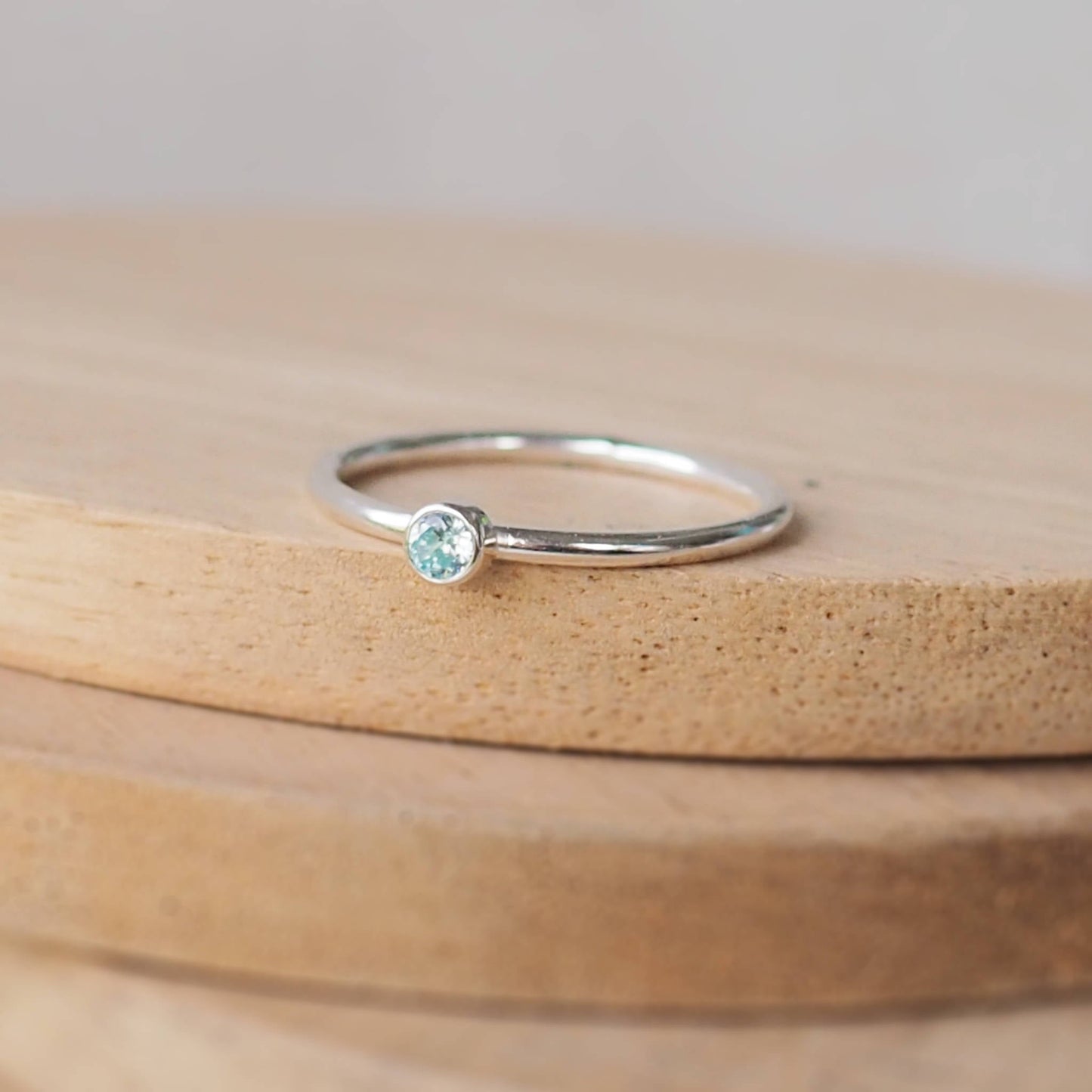 Aquamarine and Sterling Silver solitaire ring with an aqua coloured  round cubic zirconia measuring 3mm in size. A very simple minimalist ring made from Sterling Silver on a halo style band. Handmade in Scotland by maram jewellery