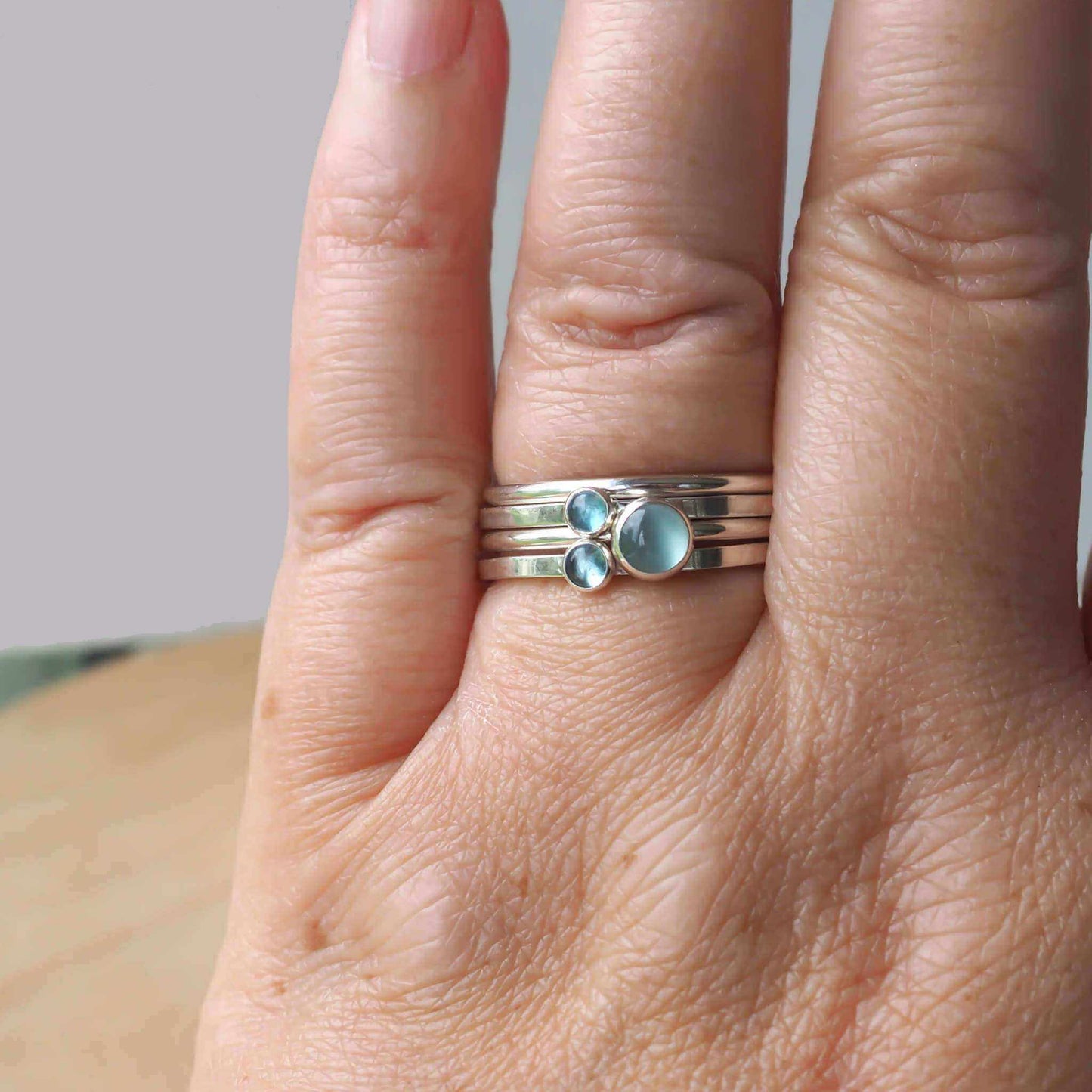 hand wearing a maram jewellery ring set with four rings, three with different sizes of aquamarine round gemstones, and a plain silver round band. Handmade by maram jewellery in Scotland