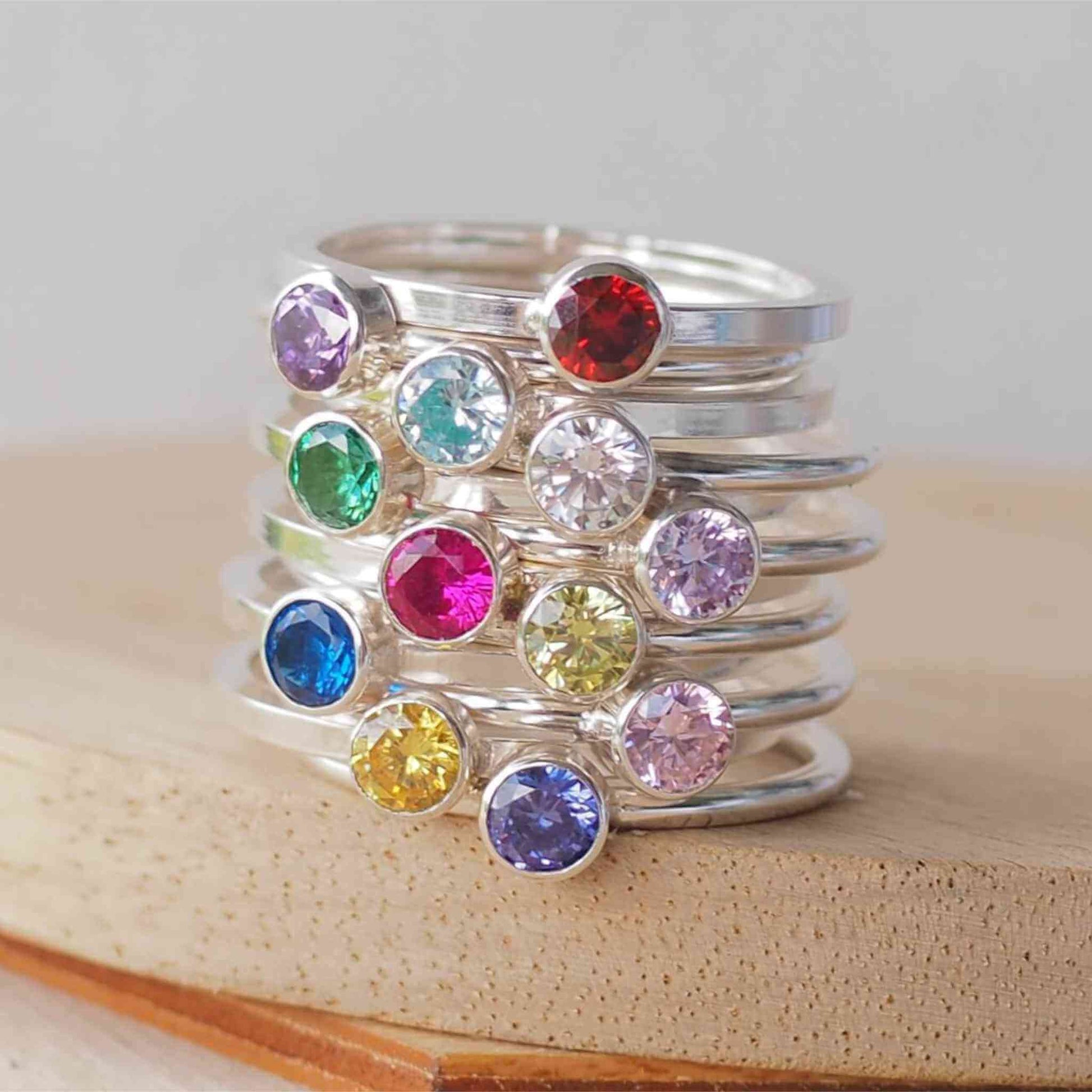 Stack of twelve birthstone rings in Sterling Silver with a round coloured cubic zirconia in 4mm size to mark birthstones for every month. Rainbow bright coloured gems with round or square silver bands to create a modern minimalist gemstone ring. Handmade in Scotland by maram jewellery