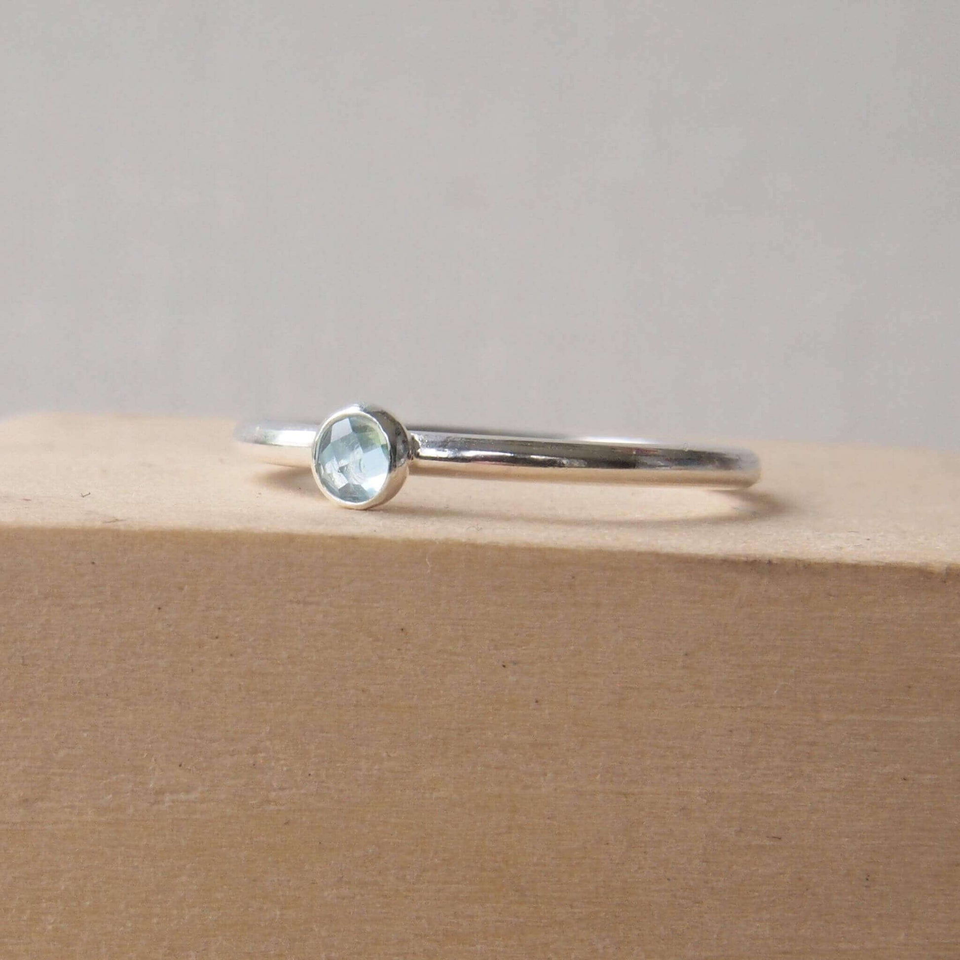 Sterling Silver and Blue topaz single gemstone ring with a small stone. The stone is a pale blue round facet cut cabochon which is simply set onto a round band of Sterling Silver. The ring is handmade to your size by Maram Jewellery