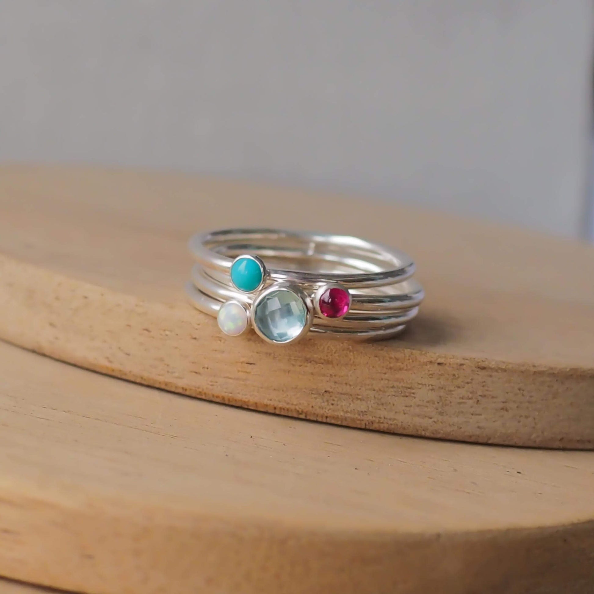 Four Ring Set with Blue Topaz, Lab Ruby, Turquoise and Lab Opal to mark March, December and October Birthdays. The four rings are made with Sterling Silver and a 5mm blue round cabochon, with three further rings with 3mm round gems in a iridescent white lab opal, turquoise, and a pinky red lab ruby. Handmade in Scotland by maram jewellery