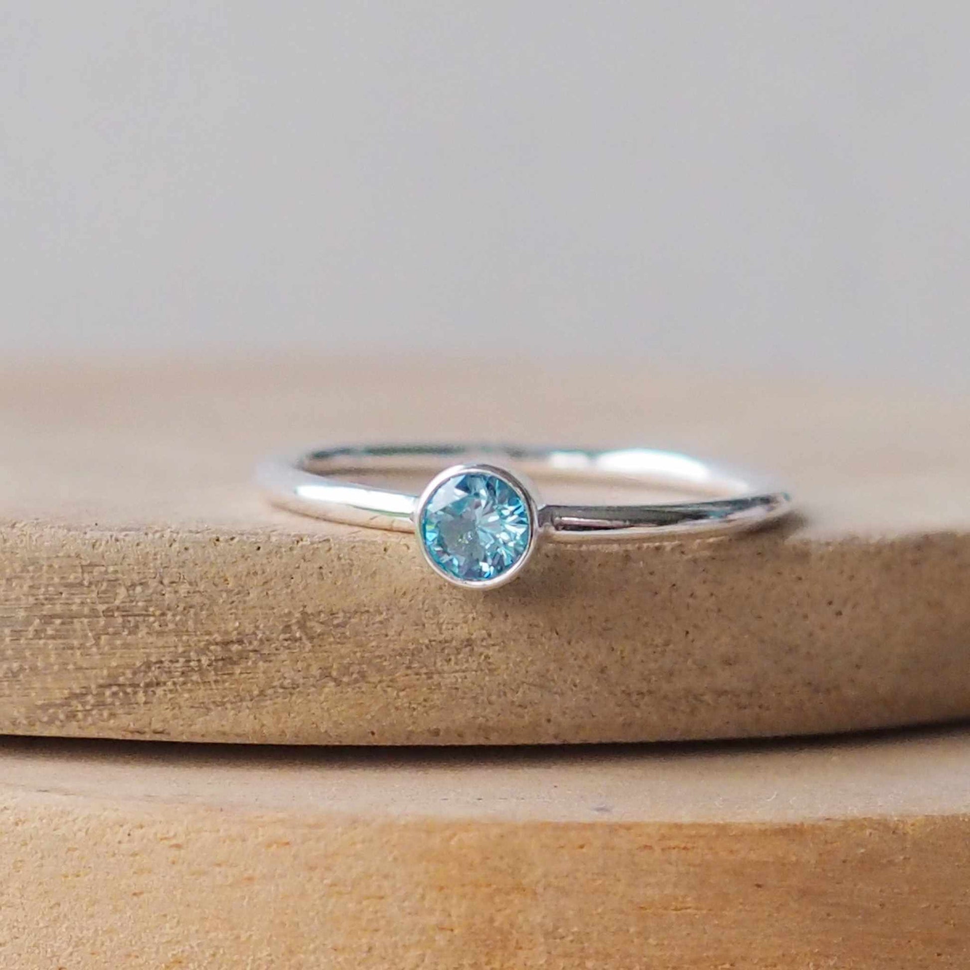 Sparkly aqua gemstone ring on white metal. Sterling Silver and Cubic zirconia ring made in a simple solitaire style with a 4mm round gemstone modern set in a fully enclosed surround. Handmade in Scotland by maram jewellery