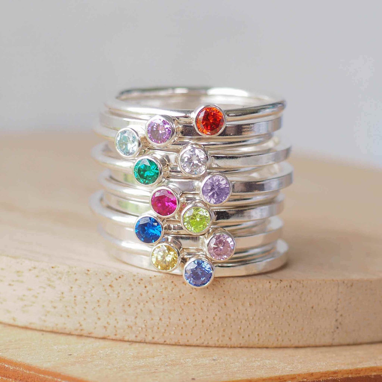 Stack of twelve birthstone rings in Sterling Silver with a round coloured cubic zirconia in 3mm size to mark birthstones for every month. Rainbow bright coloured gems with round or square silver bands to create a modern minimalist gemstone ring. Handmade in Scotland by maram jewellery