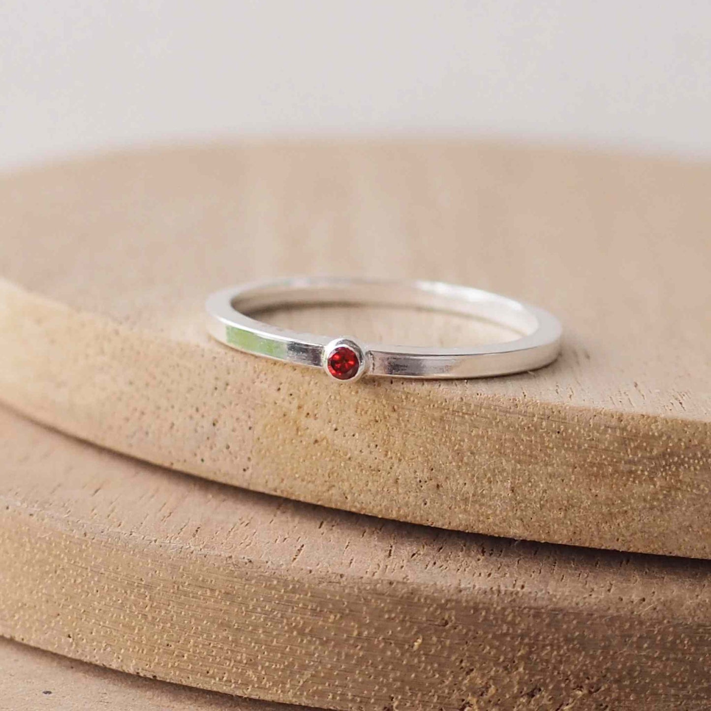 Garnet and Sterling Silver solitaire ring with a deep red coloured round cubic zirconia measuring 2mm in size. A very simple minimalist ring made from Sterling Silver on a minimalist square style band. Handmade in Scotland by maram jewellery