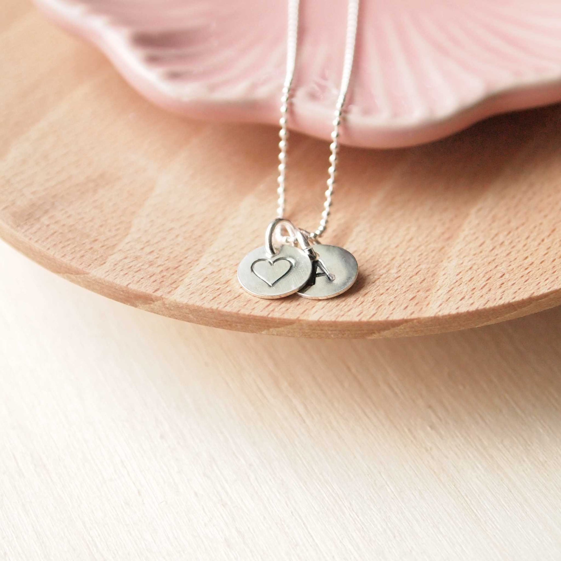 Silver letter and heart token charms on a simple silver chain. Subtle and understated necklace handmade by maram jewellery in UK