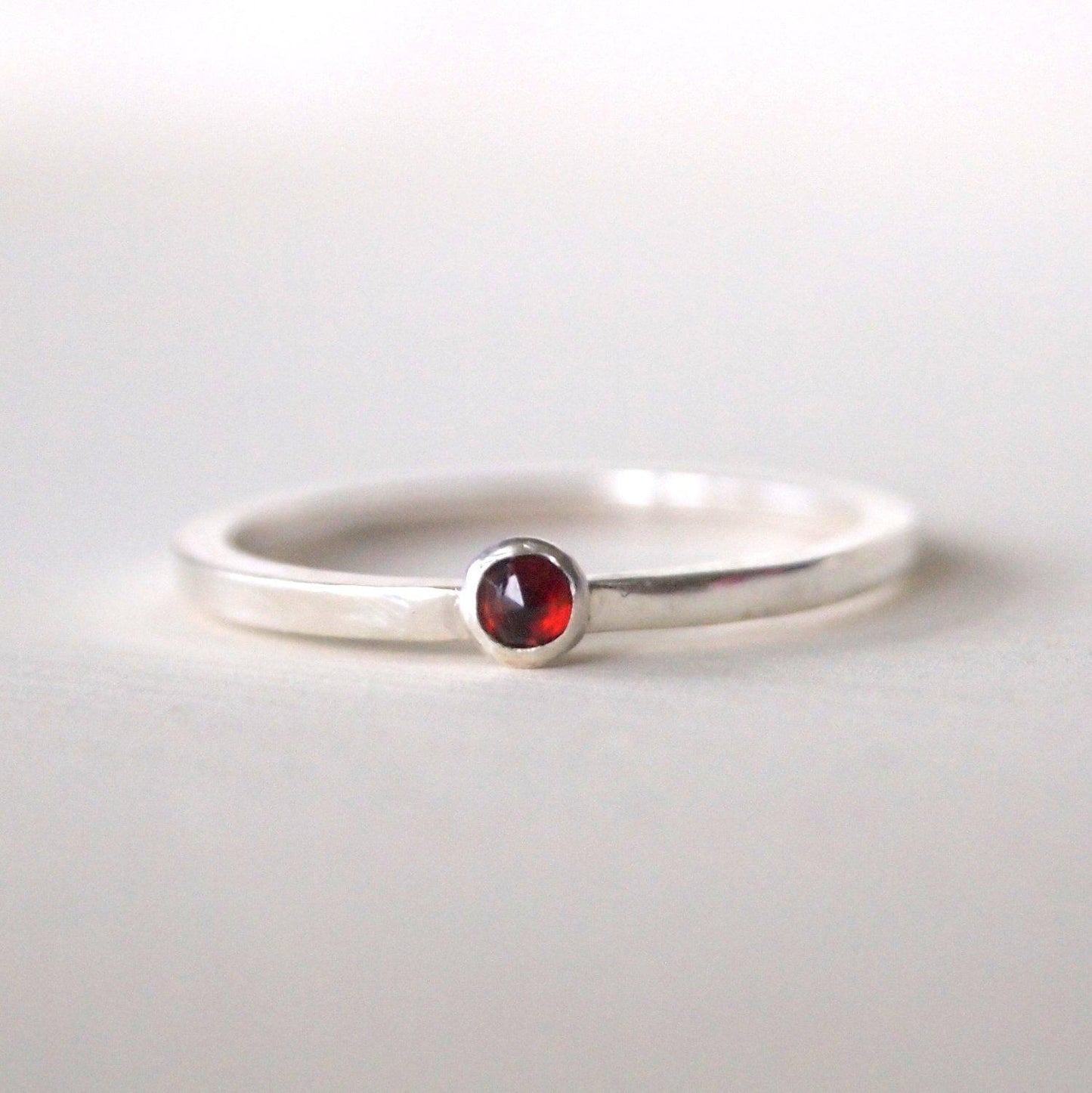 Garnet and Sterling Silver Birthstone Ring for January. The ring is simple in style on a plain square band with a small round facet dark red garnet in the centre. The ring is handmade to your size by maram jewellery in Scotland