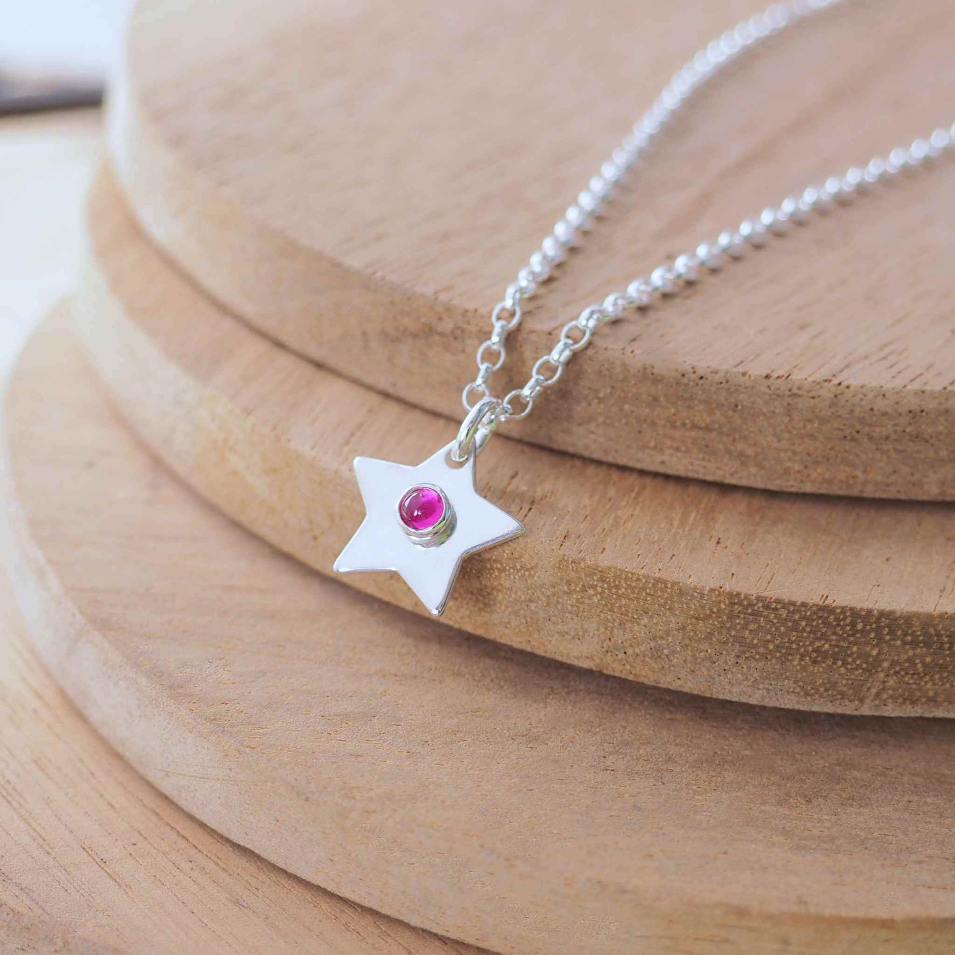 July Birthstone Charm Necklace in the shape of a star with a round 3mm lab ruby cabochon centre. The star measures 12mm in size so is small enough for children as well as adults and is available in a range of other birthstones too. It is Sterling Silver and comes with a choice of chain design and length. Handmade in Scotland by Maram Jewellery