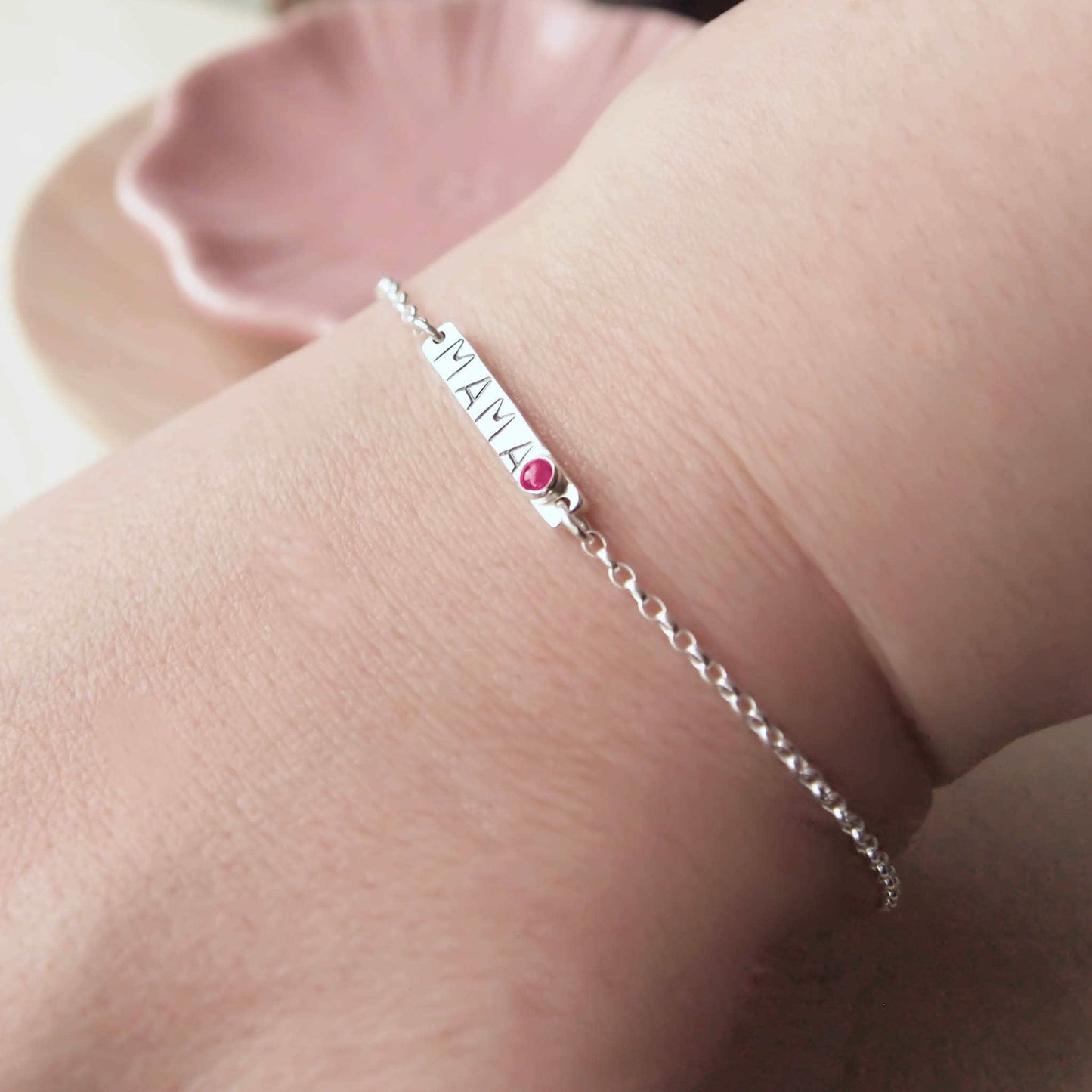 Silver Bar bracelet with hand stamped MAMA with a baby birthstone in July Lab Ruby. Worn on hand to show size.Handmade by maram jewellery in Scotland UK