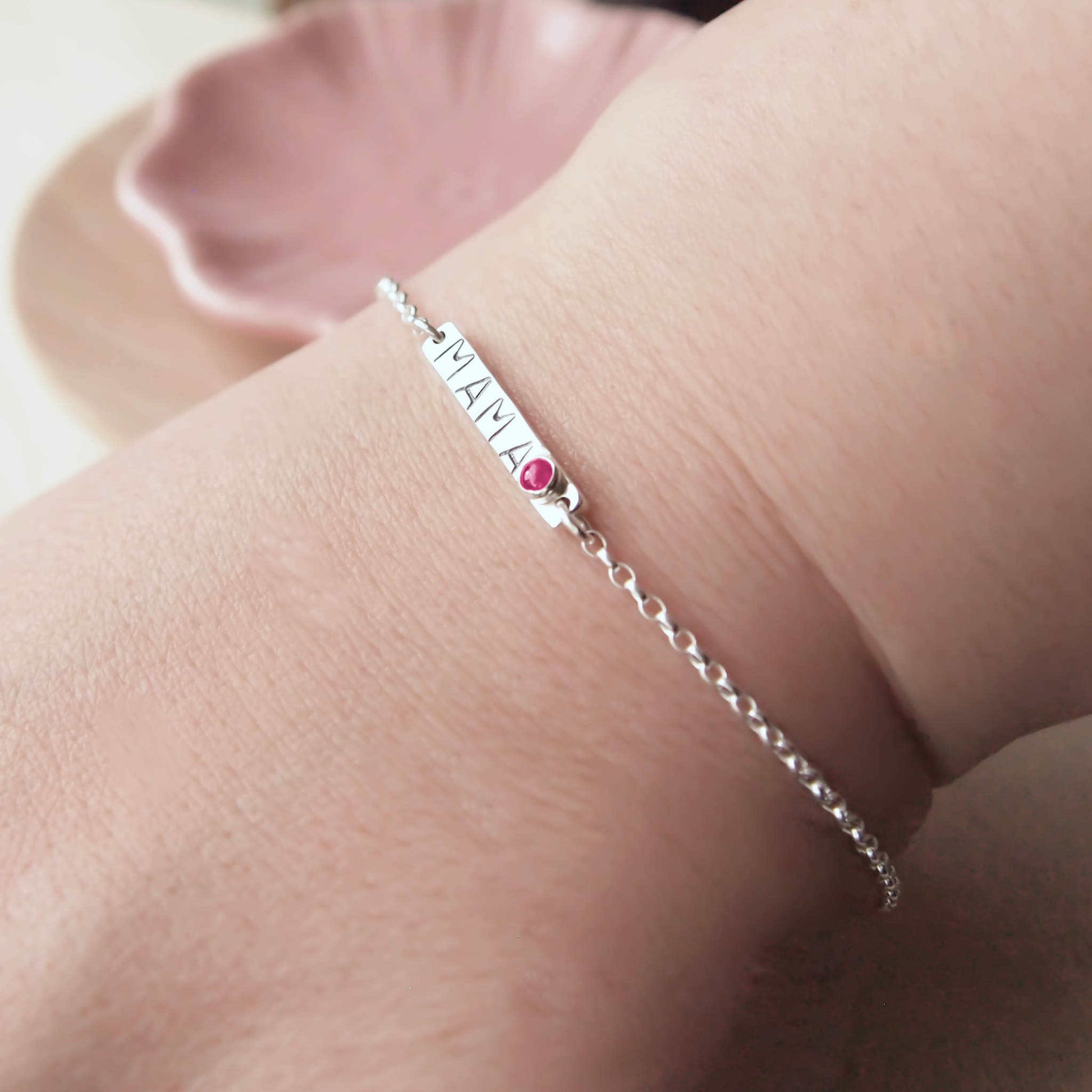 Silver Bar bracelet with hand stamped MAMA with a baby birthstone in July Lab Ruby. Worn on hand to show size.Handmade by maram jewellery in Scotland UK