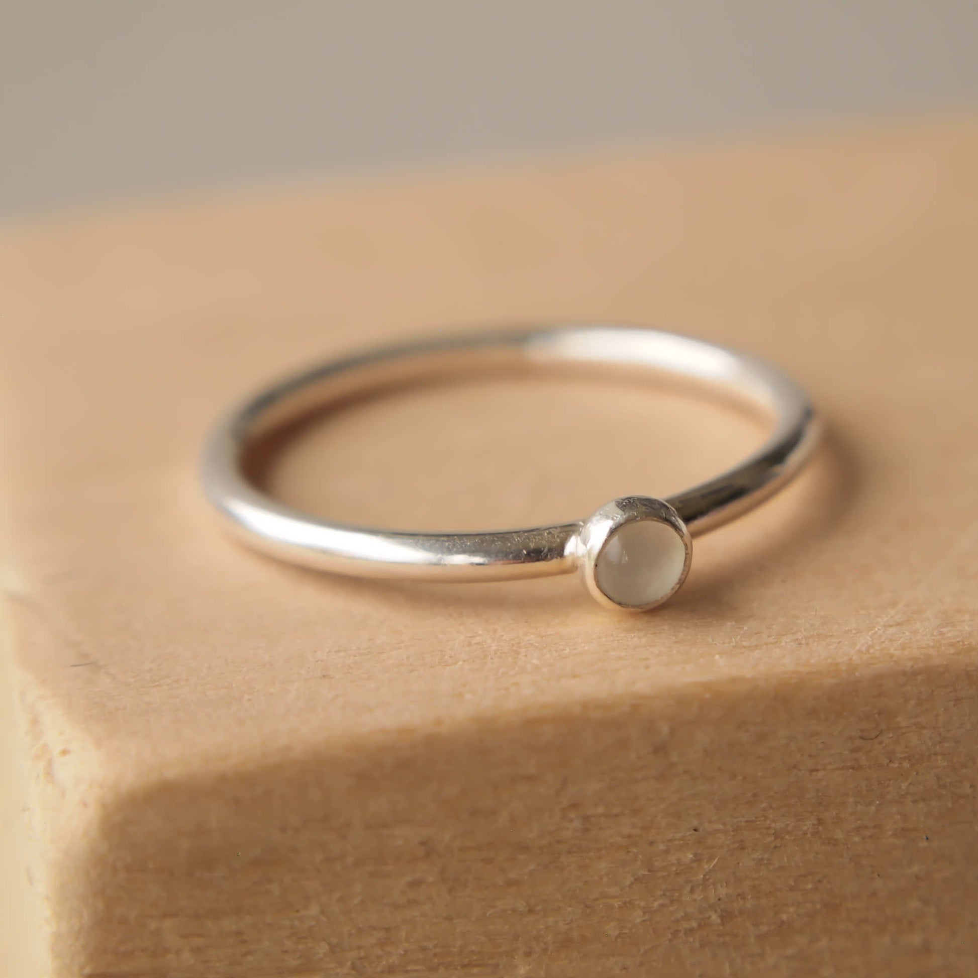 Sterling silver and moonstone cabochon ring worn on hand. 3mm sized milky white cabochon stone on a square band of sterling silver. Handmade in Scotland by maram jewellery