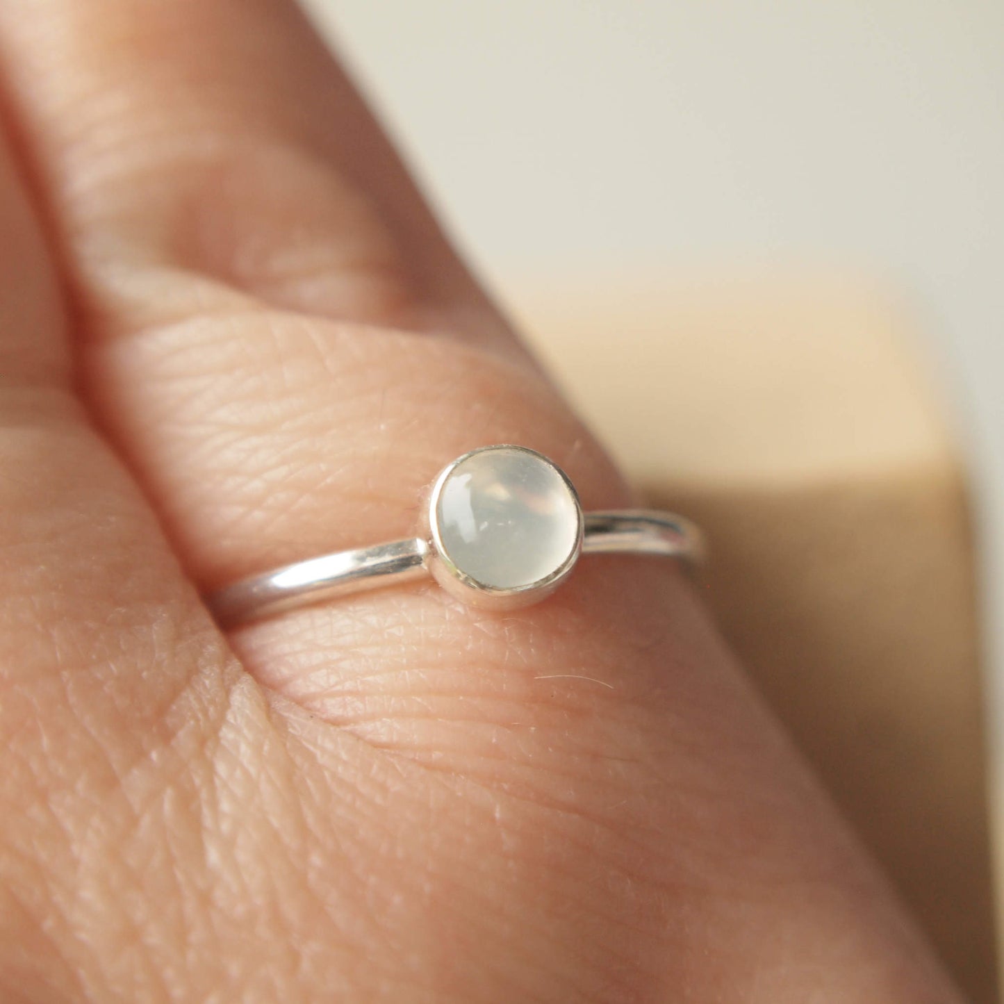 Sterling silver and moonstone cabochon ring worn on hand. 5 mm sized milky white cabochon stone on a fully round band of sterling silver. Handmade in Scotland by maram jewellery