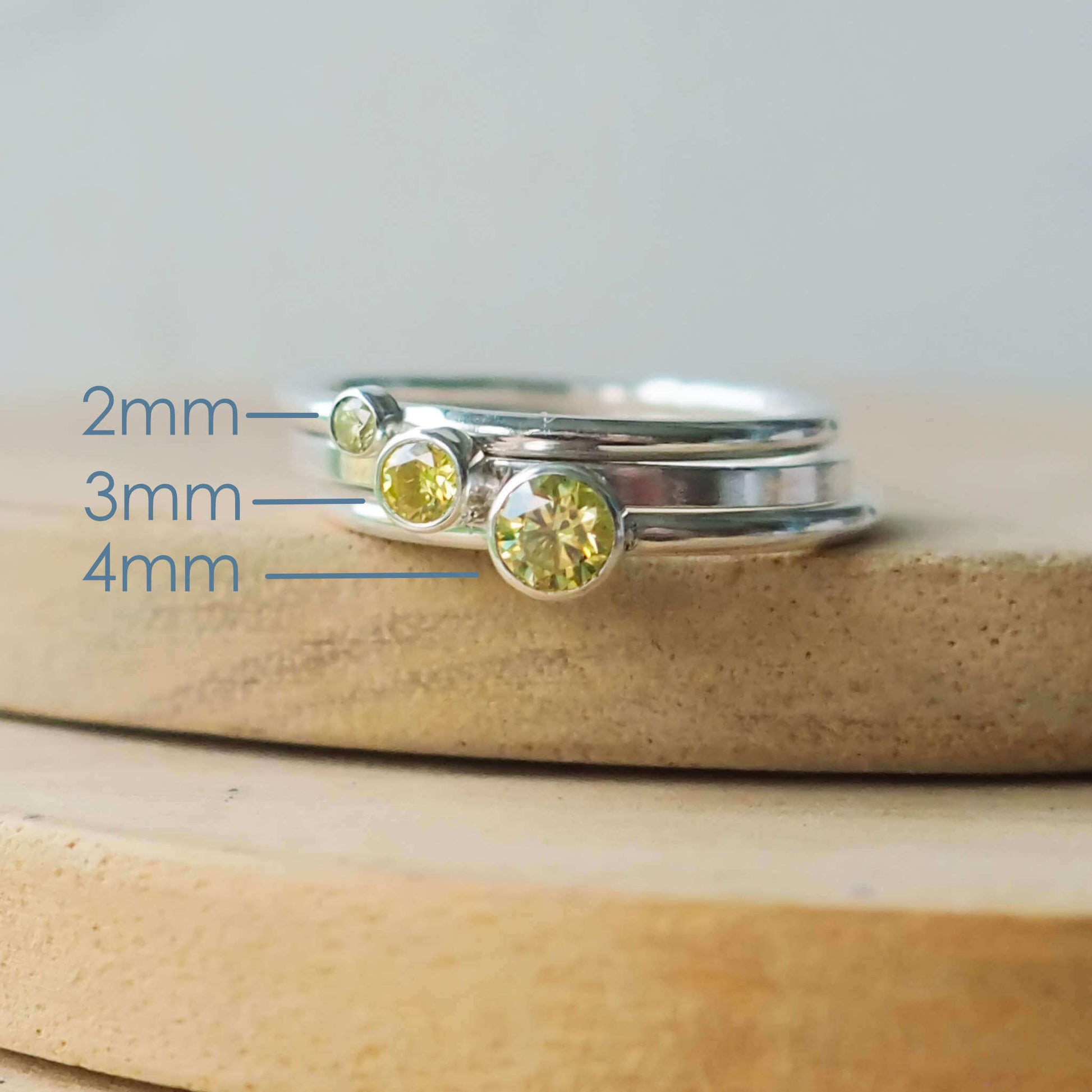 Three rings showing the square and round band styles with three different sized Cubic Zirconia in a light moss green Peridot. The rings are made from Sterling Silver and a round pale green cubic zirconia measuring 2,3 or 4mm in size. Handmade by maram jewellery in Scotland