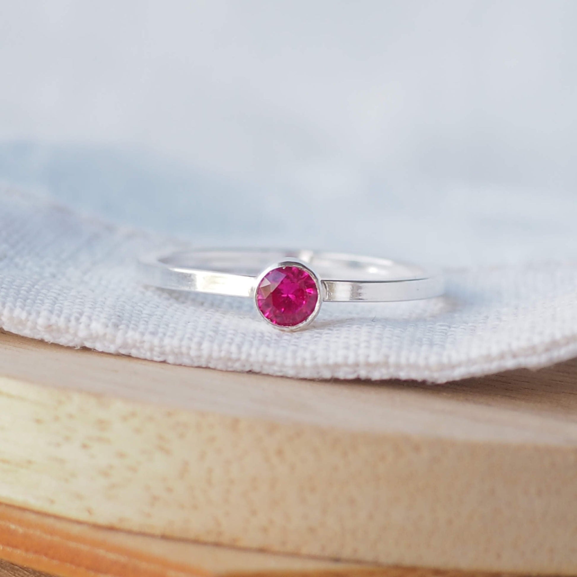 Silver ring with a pinky red gemstone. The ring is simple in style with no embellishment , with a round wire band 1.5mm thick with a simple ruby coloured 4mm round cubic zirconia stone set in an enclosed silver setting. Ruby is birthstone for July. The ring is Sterling Silver and made to your ring size. Handmade in Scotland by Maram Jewellery