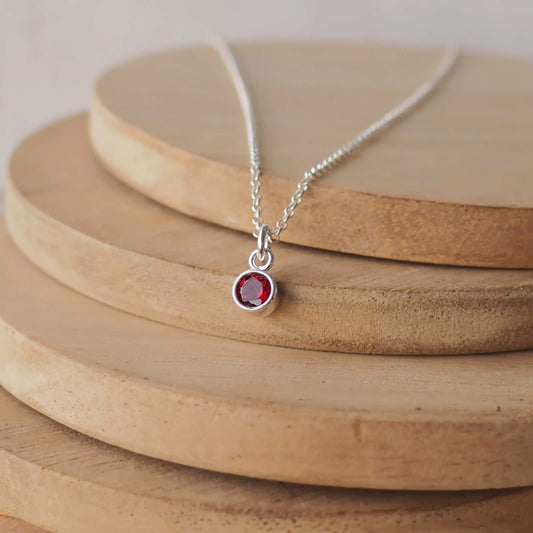 Petite Sterling Silver and Cubic Zirconia necklace with Ruby Birthstone. A small 4mm faceted round red gemstone with a simple silver setting on a trace style chain. Handmade in Scotland by Maram Jewellery