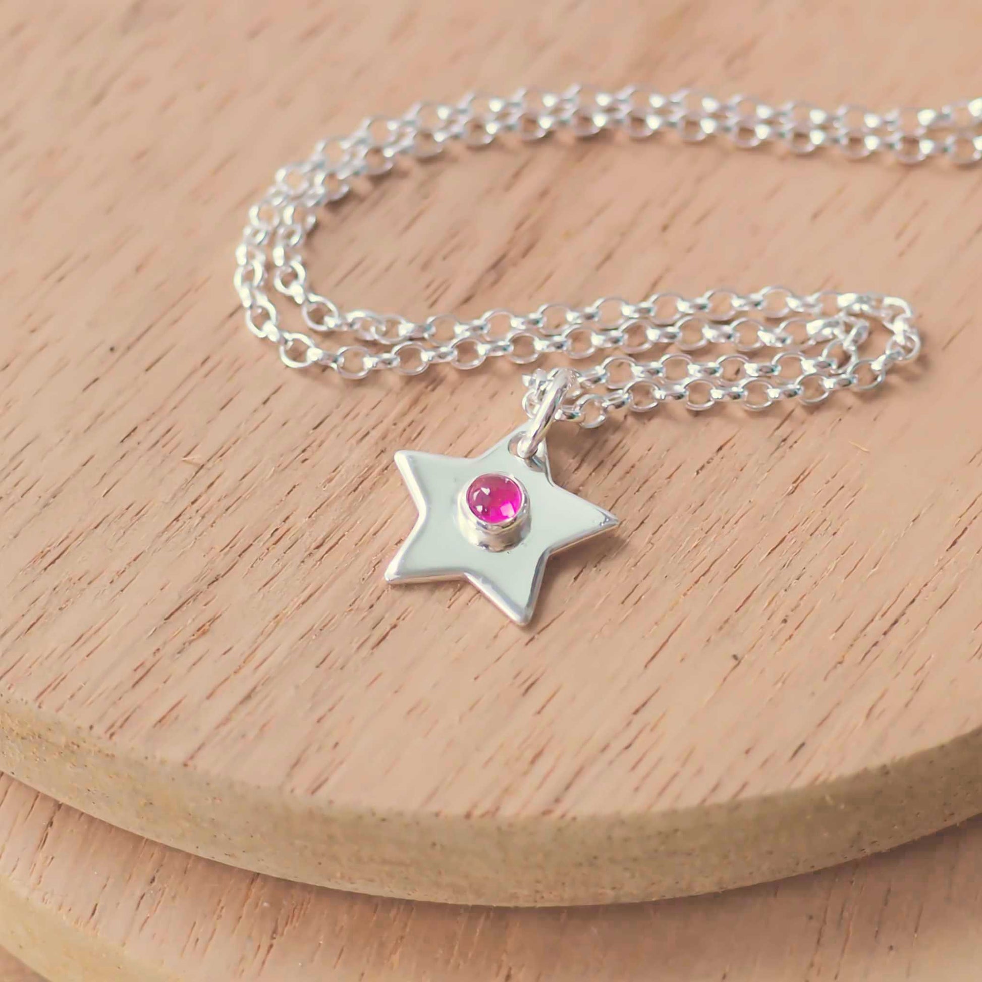 July Birthstone Charm Necklace in the shape of a star with a round 3mm lab ruby cabochon centre. The star measures 12mm in size so is small enough for children as well as adults and is available in a range of other birthstones too. It is Sterling Silver and comes with a choice of chain design and length. Handmade in Scotland by Maram Jewellery