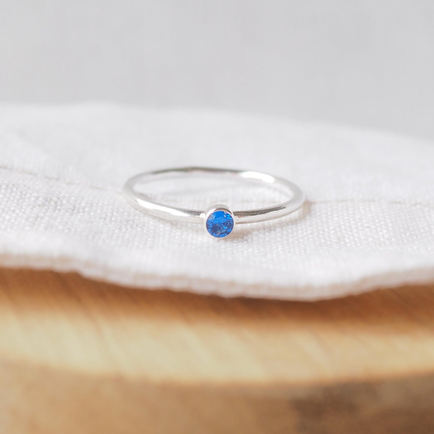 Silver ring with a bright blue gemstone. The ring is simple in style with no embellishment , with a round wire band 1.5mm thick with a simple blue sapphire 3mm round cubic zirconia stone set in an enclosed silver setting. Sapphire is birthstone for September. The ring is Sterling Silver and made to your ring size. Handmade in Scotland by Maram Jewellery