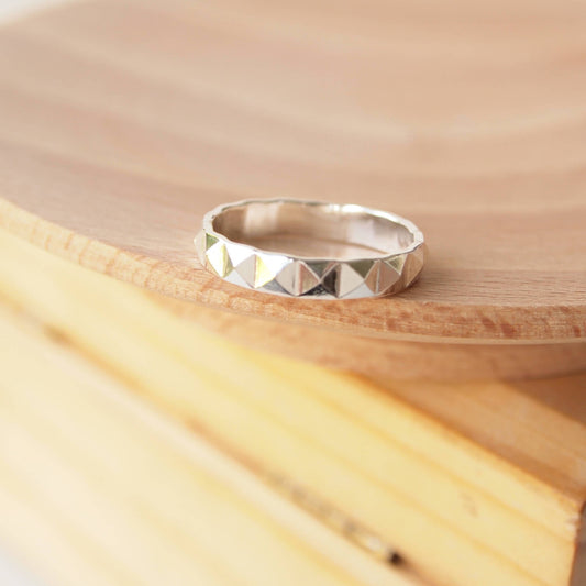 SIlver unisex ring with a wide band and a pyramid pattern pictured on a wooden background. Handmade by maram jewellery in Scotland