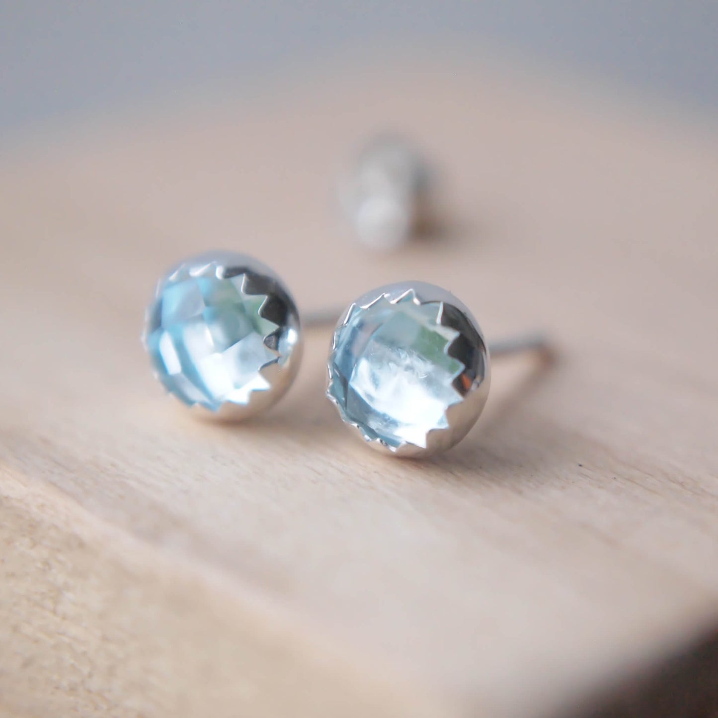 March Birthstone Blue Topaz Earrings in a pale blue facet cut gemstone with a simple silver surround with a jagged edge. Handmade in Scotland by maram jewellery