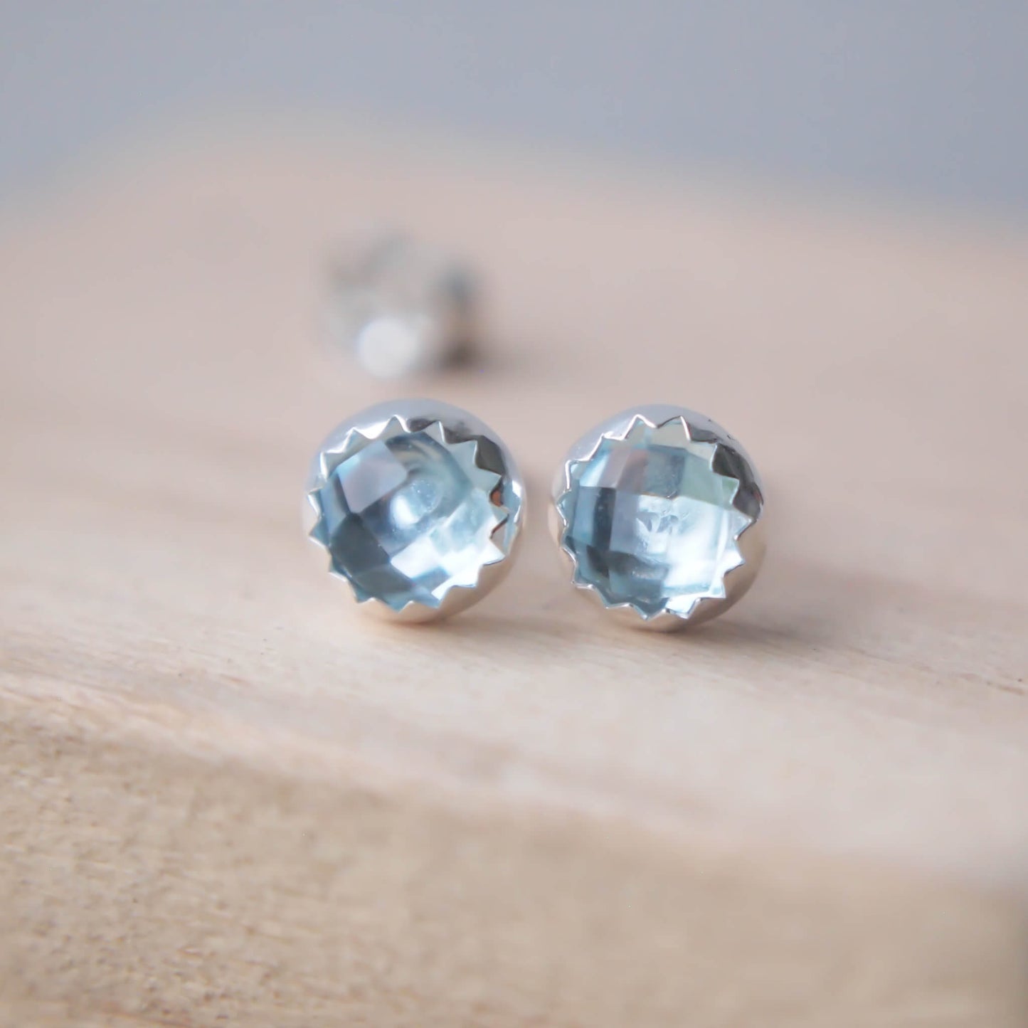 March Birthstone Blue Topaz Earrings in a pale blue facet cut gemstone with a simple silver surround with a jagged edge. Handmade in Scotland by maram jewellery