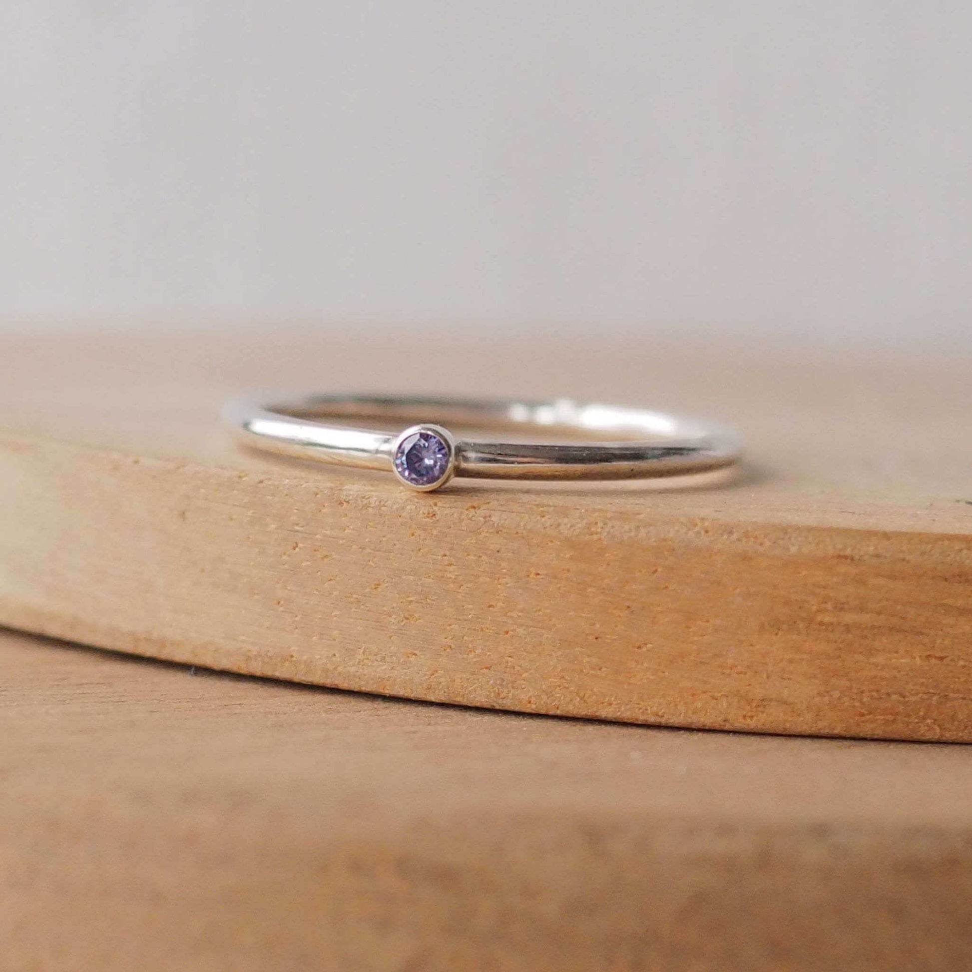 Silver ring with a light purple gemstone. The ring is simple in style with no embellishment , with a round wire band 1.5mm thick with a simple Tanzanite 2mm round cubic zirconia stone set in an enclosed silver setting. The gem is very small and minimal on the band. Tanzanite is birthstone for December. The ring is Sterling Silver and made to your ring size. Handmade in Scotland by Maram Jewellery